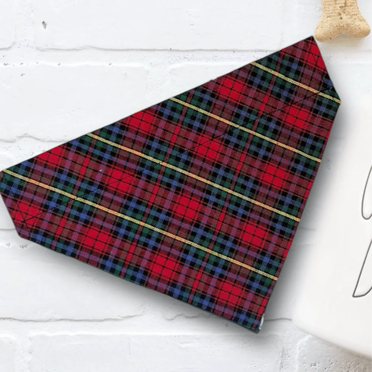 Red plaid Christmas dog bandana with gold lines shown on a white brick backdrop