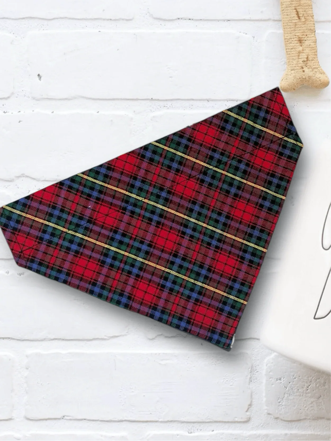 Red plaid Christmas dog bandana with gold lines shown on a white brick backdrop