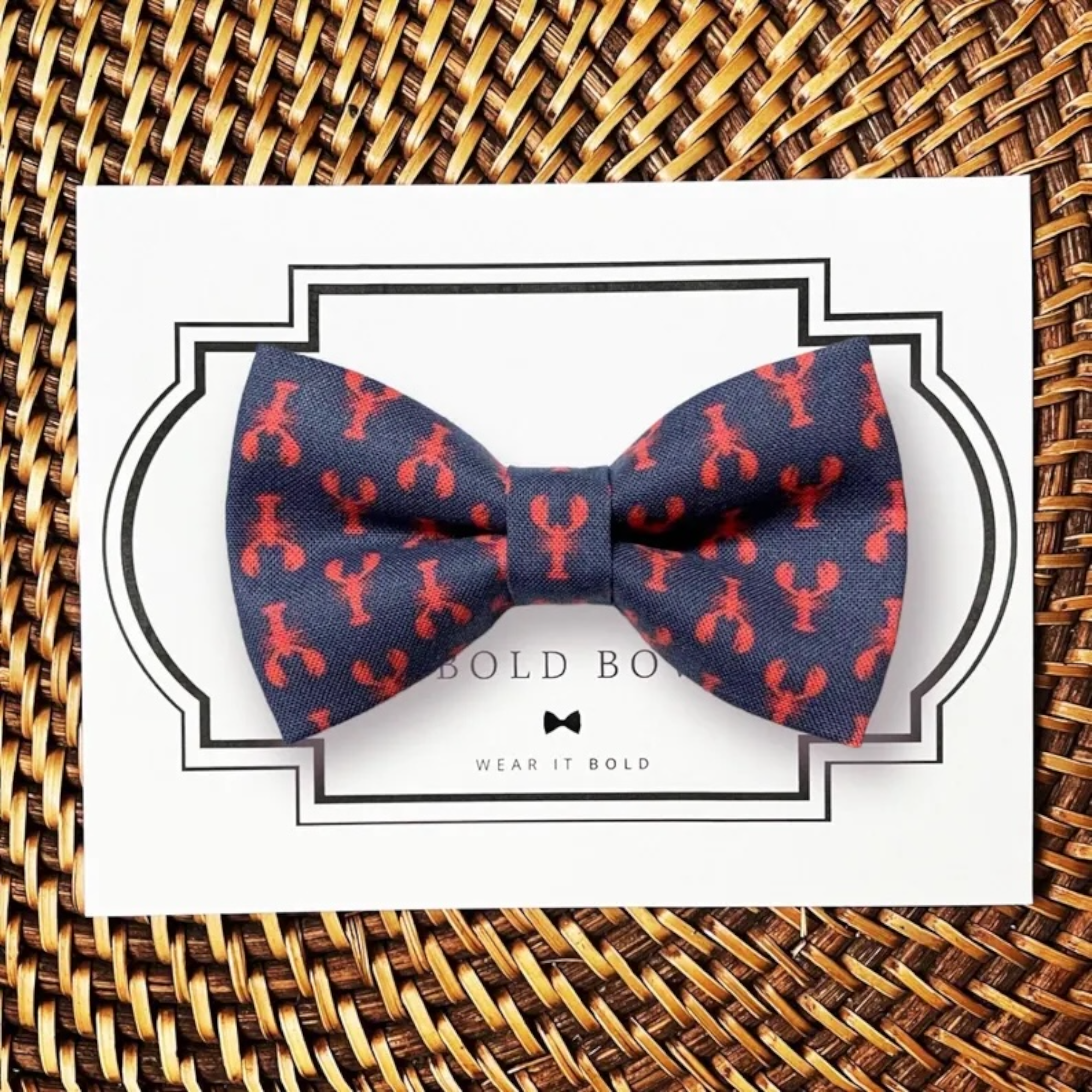 Navy blue dog bow tie with red lobster pattern on a card, placed on a woven surface.