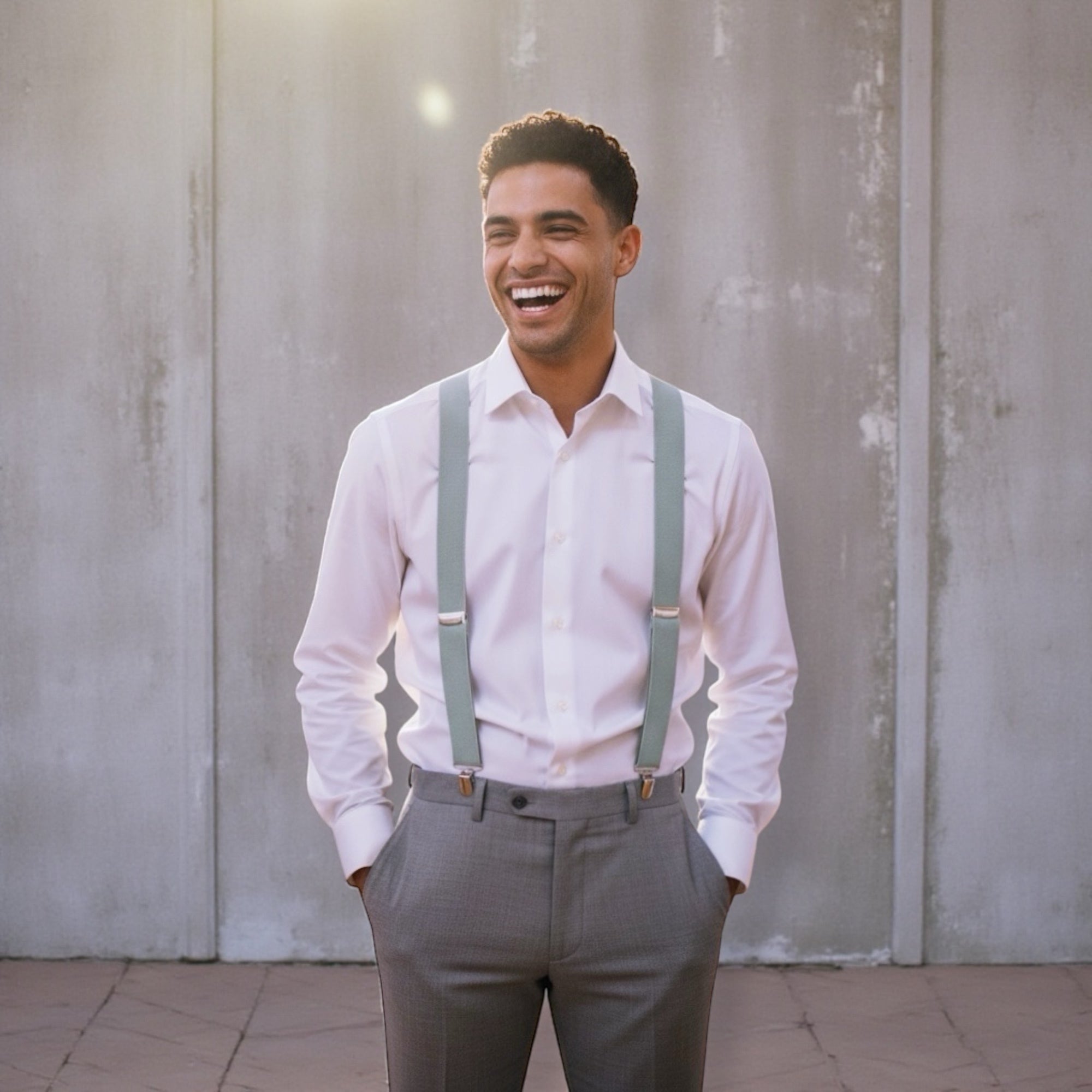 Groomsman in a white shirt and gray pants with Sage green suspenders laughing in a wedding reception setting.
