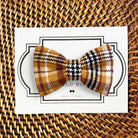 A mustard yellow and gold plaid dog bow tie displayed on a card with 'The Bold Bow Tie' branding.
