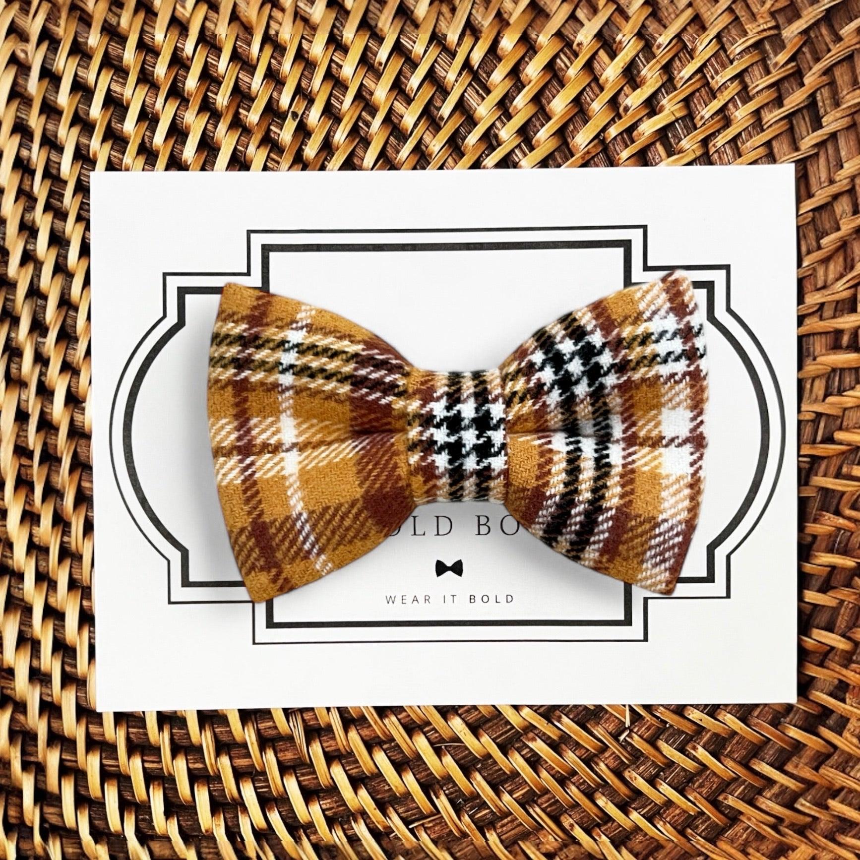 A mustard yellow and gold plaid dog bow tie displayed on a card with 'The Bold Bow Tie' branding.