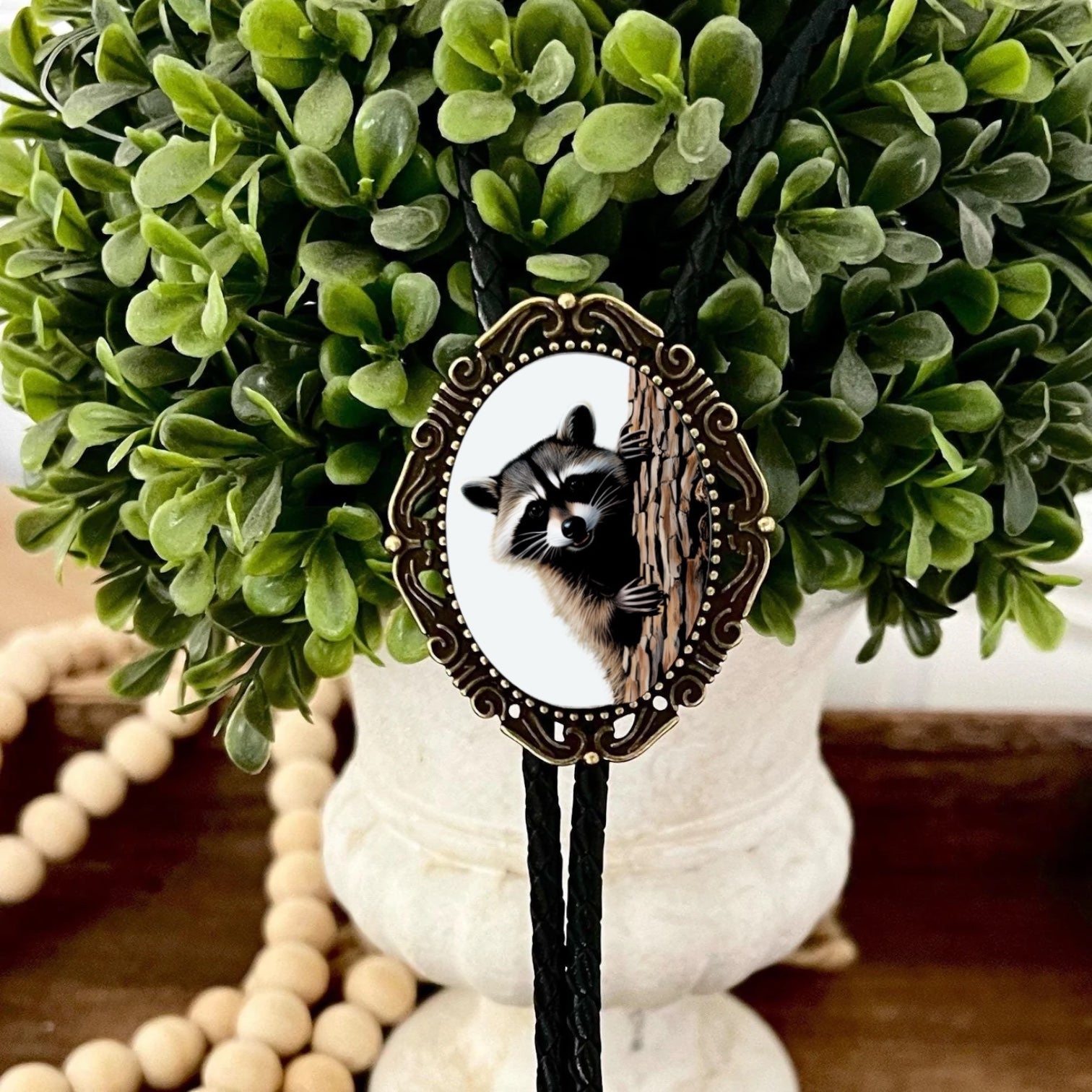 Western Bolo Tie with Raccoon with black leather cord decorative green boxwood arrangement.