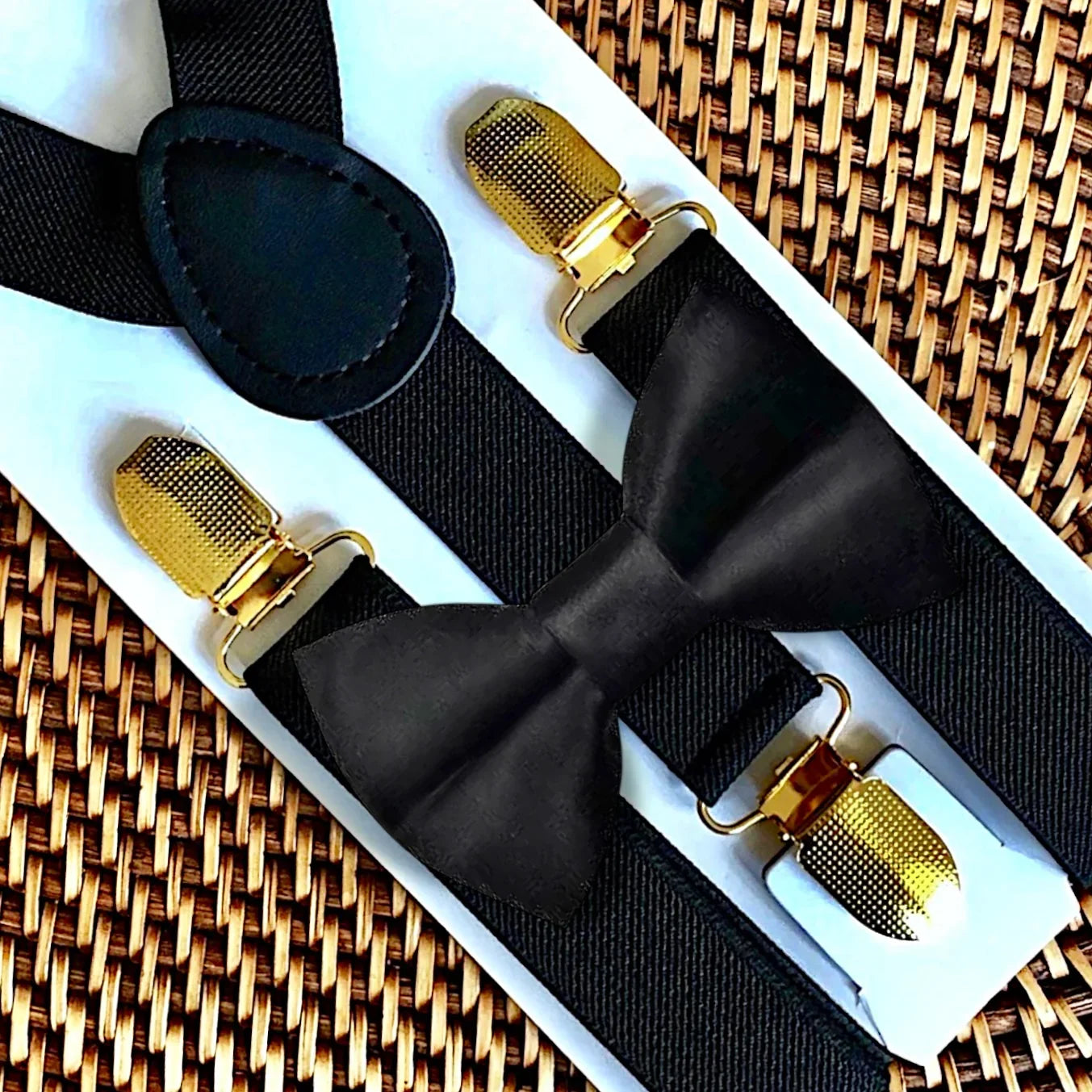 Black bow tie and suspenders with gold clasps on a woven surface