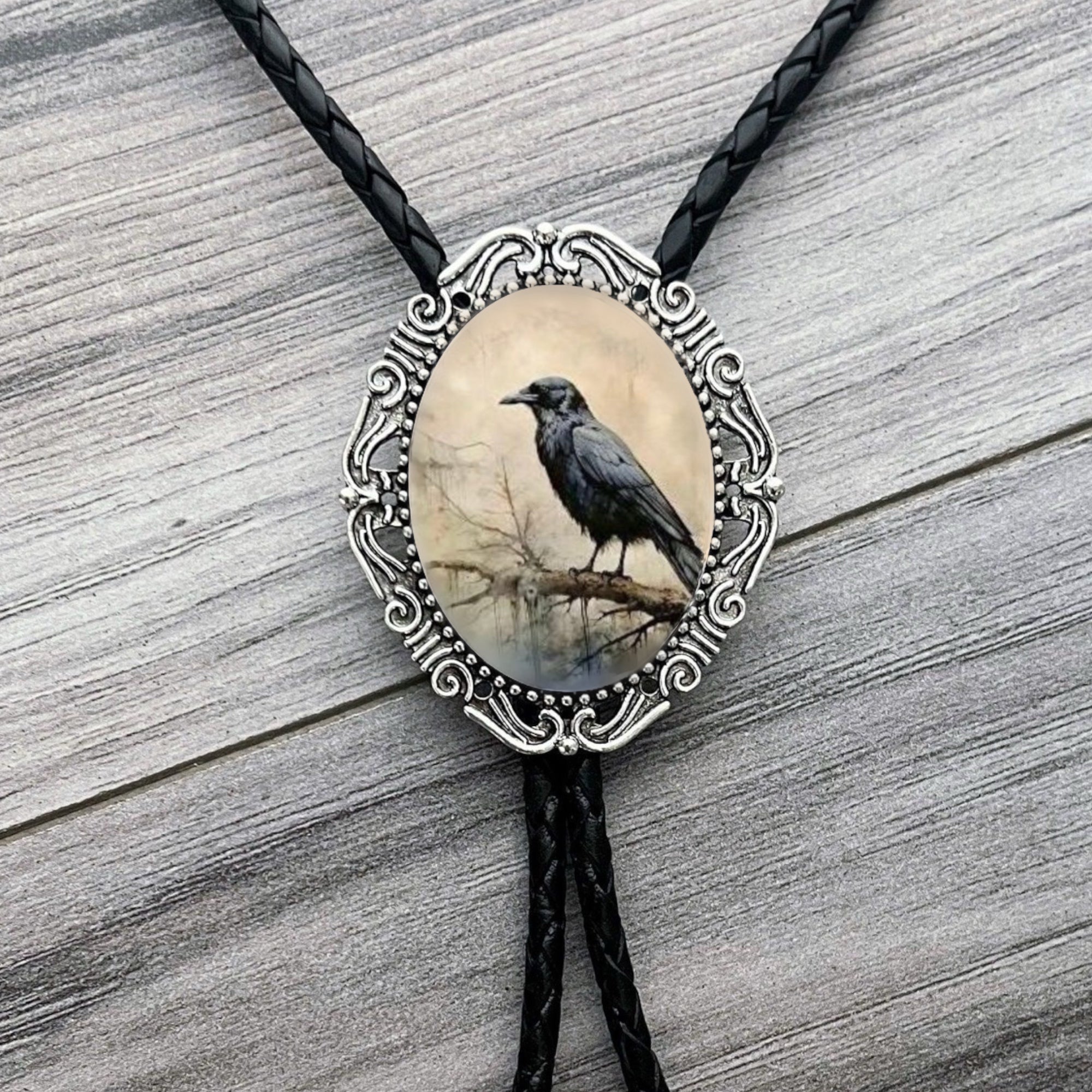 Raven Bolo tie with a black crow design on an oval pendant against a wooden background