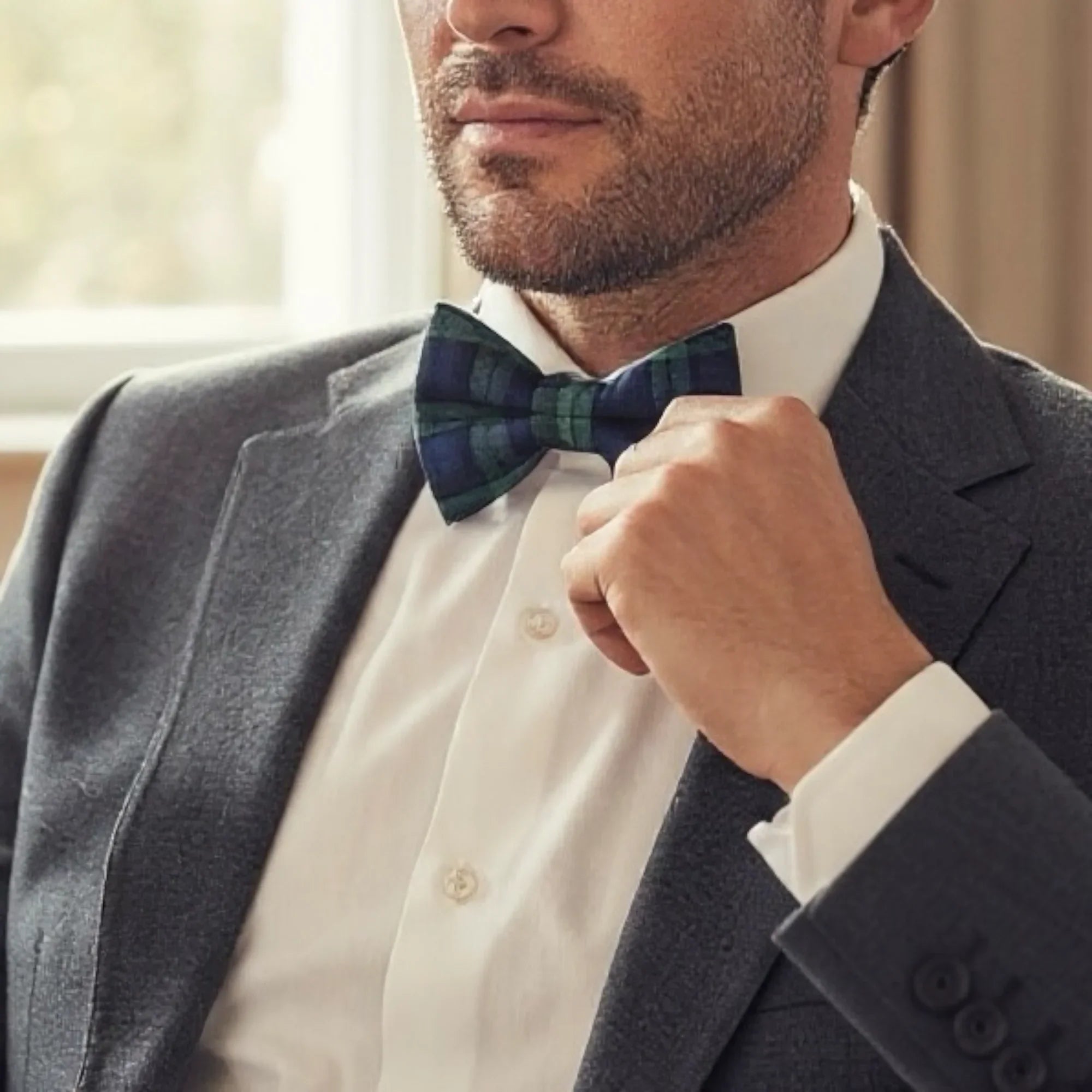 Plaid bow tie in navy and green check worn by a man in a suit.