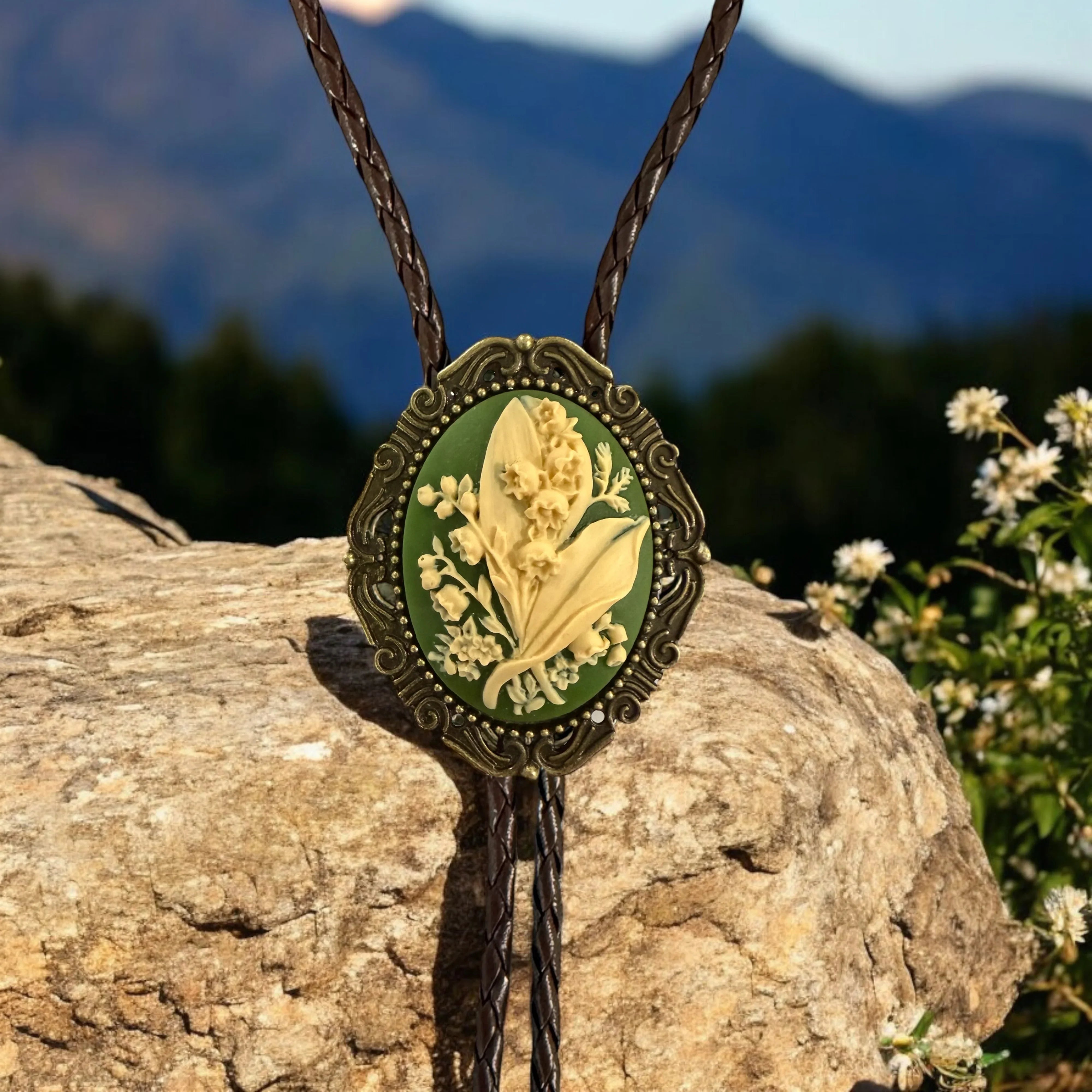 Decorative green lily of the valley with floral design bolo tie on a rock with mountain background