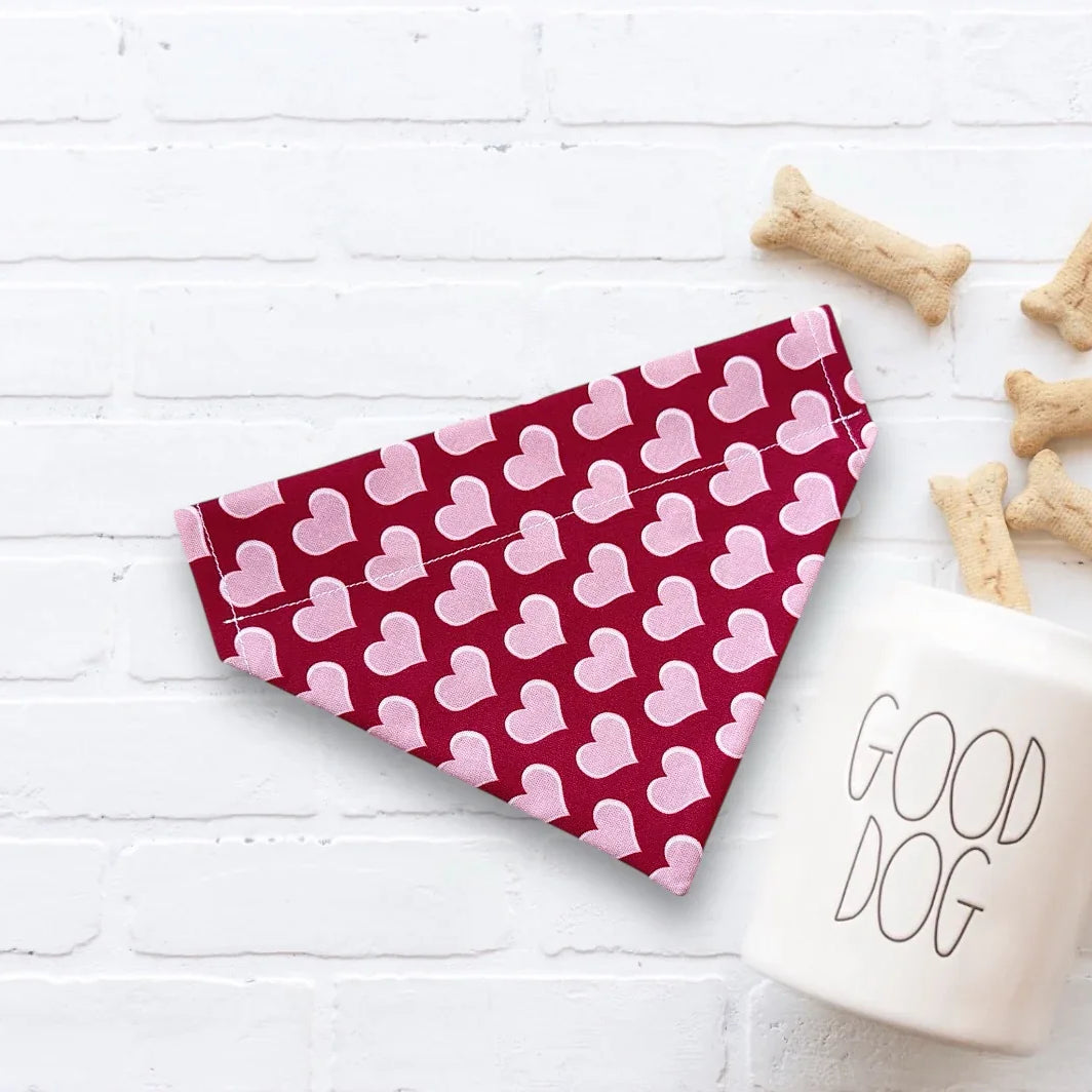 Red and pink heart dog bandana for Valentine’s Day next to a 'Good Dog' mug on a white surface.