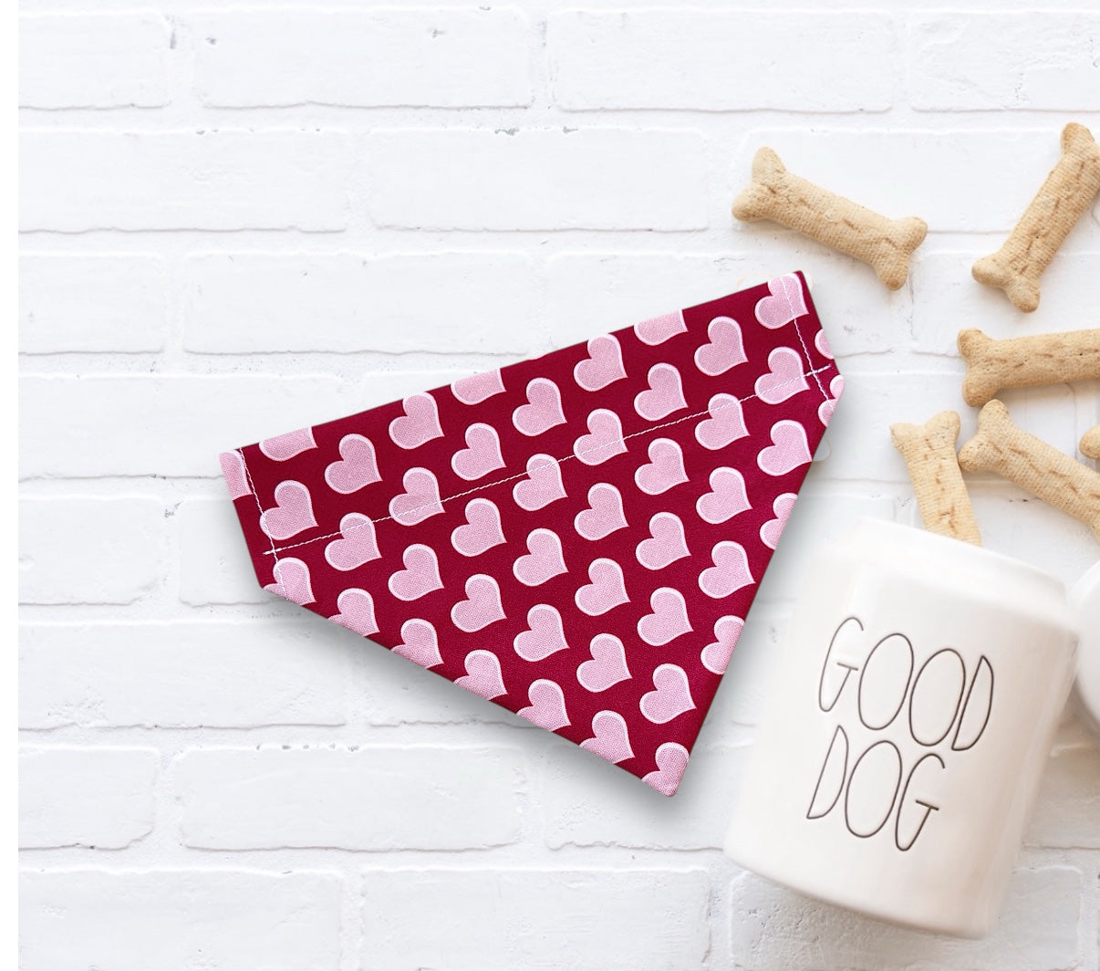 Red and pink heart dog bandana for Valentine’s Day next to a 'Good Dog' mug on a white surface.