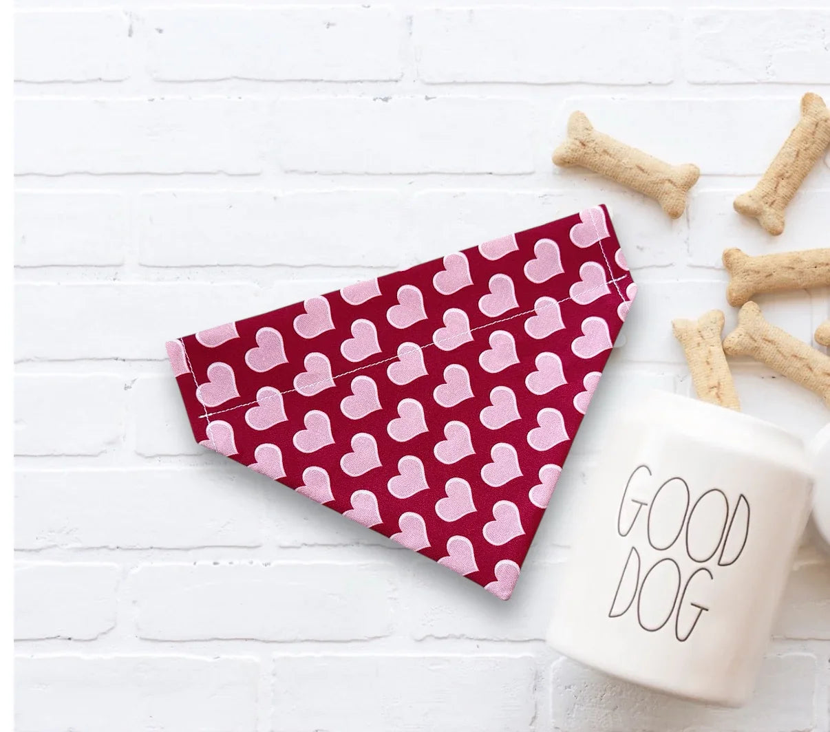 Red and pink heart dog bandana for Valentine’s Day next to a 'Good Dog' mug on a white surface.