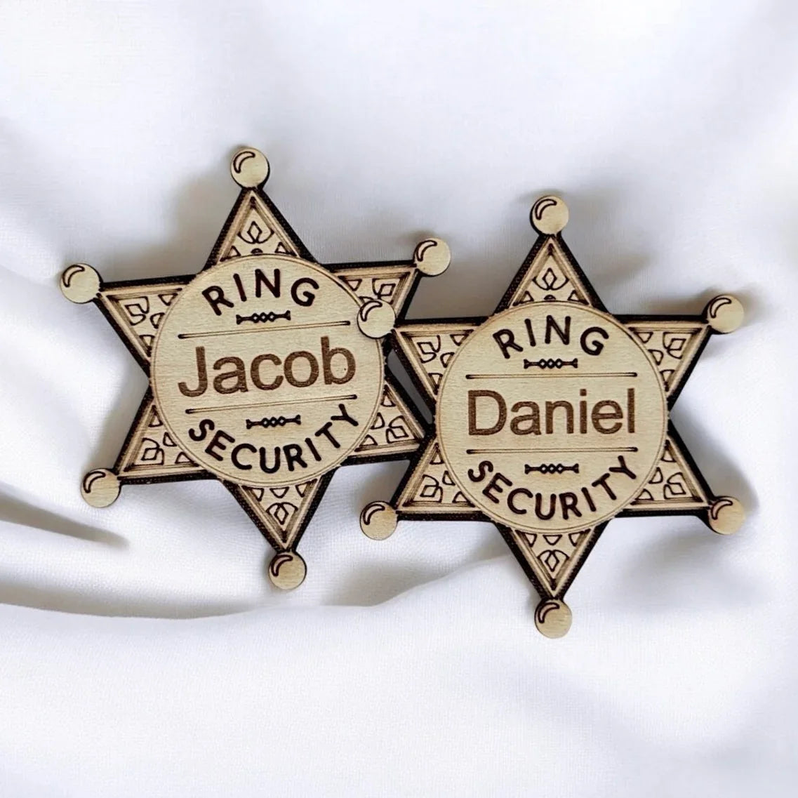 Two personalized wooden ring bearer badges in star shapes with the names Jacob and Daniel for a wedding.