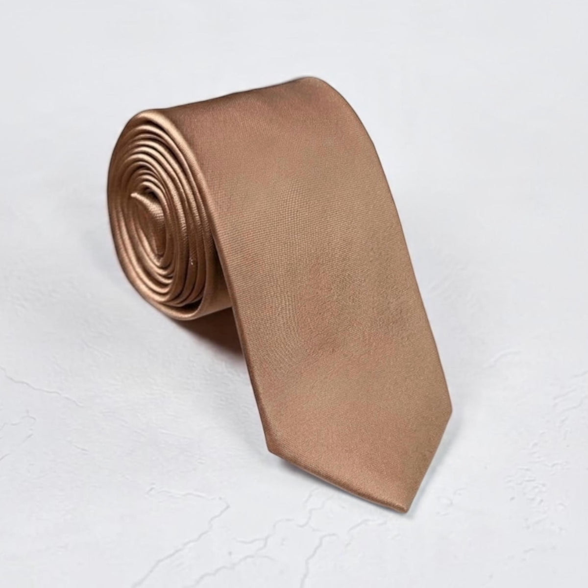 A rolled-up taupe necktie in a warm metallic bronze or copper tone, displayed on a light textured white background.