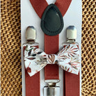 Burnt orange suspenders with floral bow ties on a woven surface
