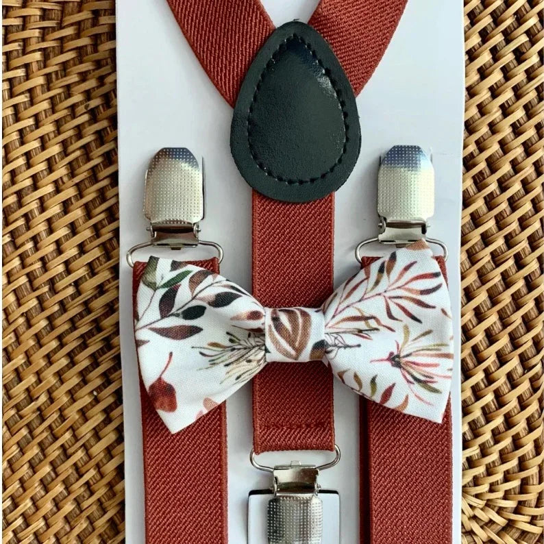 Burnt orange suspenders with floral bow ties on a woven surface