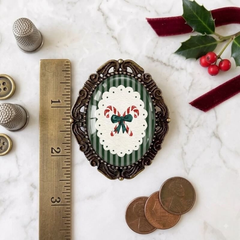 Holiday-themed brooch with candy cane bow on green stripes, vintage frame, sewing tools & holly nearby