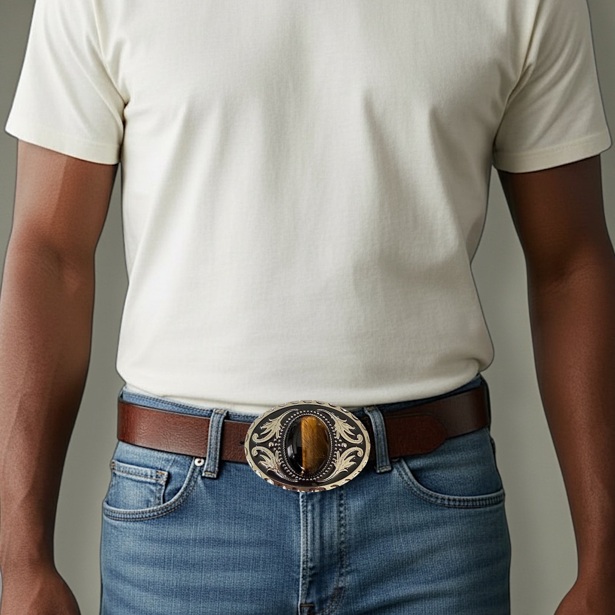 Man wearing a white t-shirt, blue jeans, and a brown belt with a decorative tiger’s eye belt buckle.