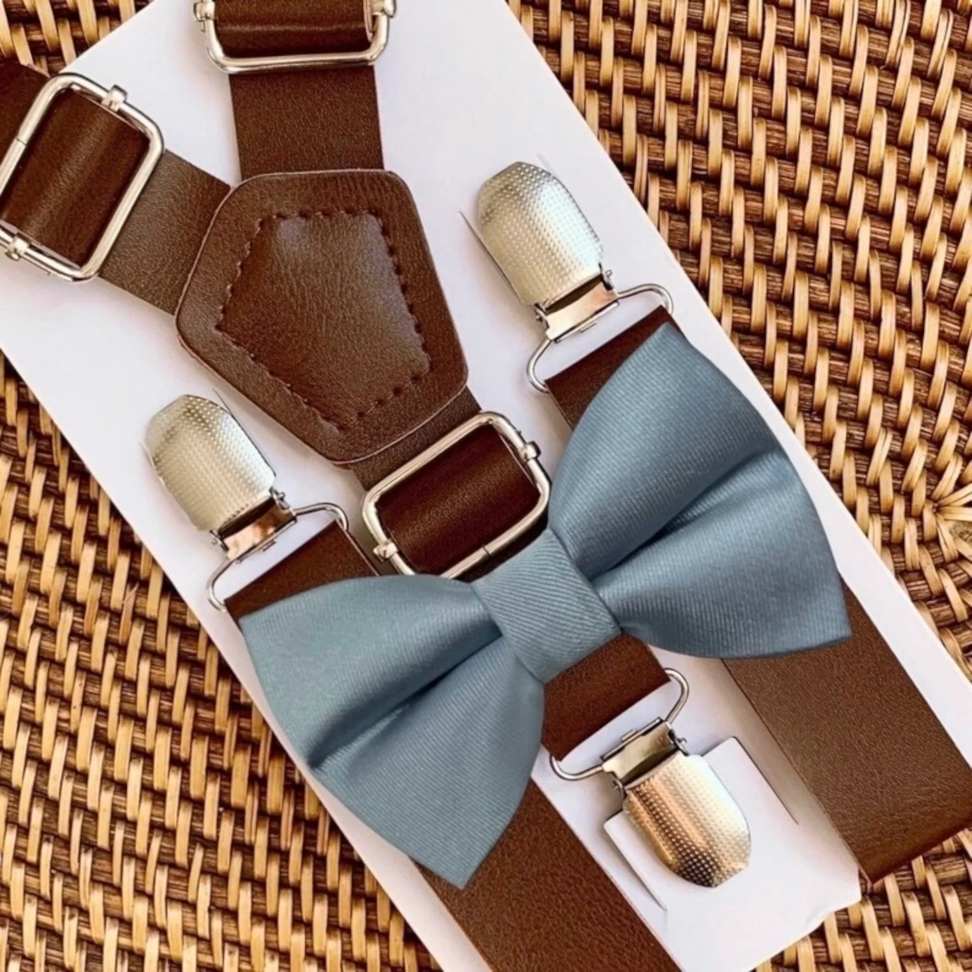 Dusty blue satin bow tie with dark brown vegan leather suspenders on a white display card