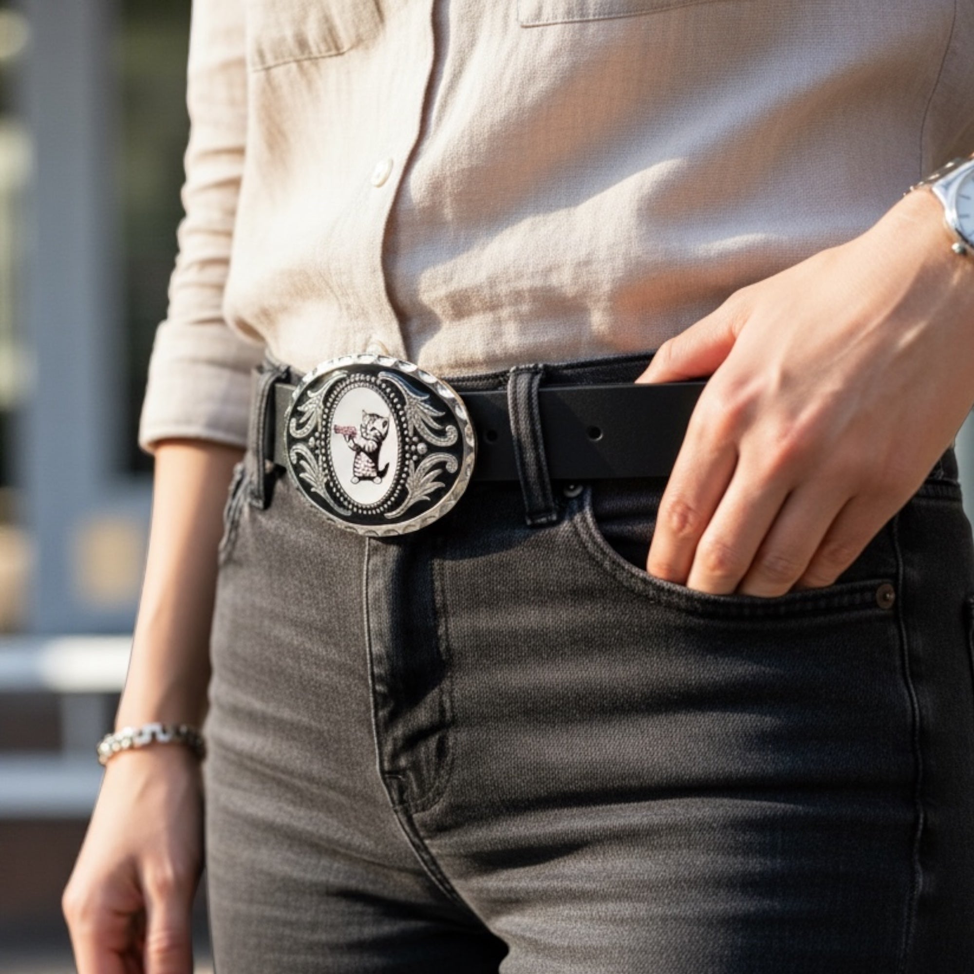 Person wearing a black belt with a decorative cat belt buckle, standing outdoors.