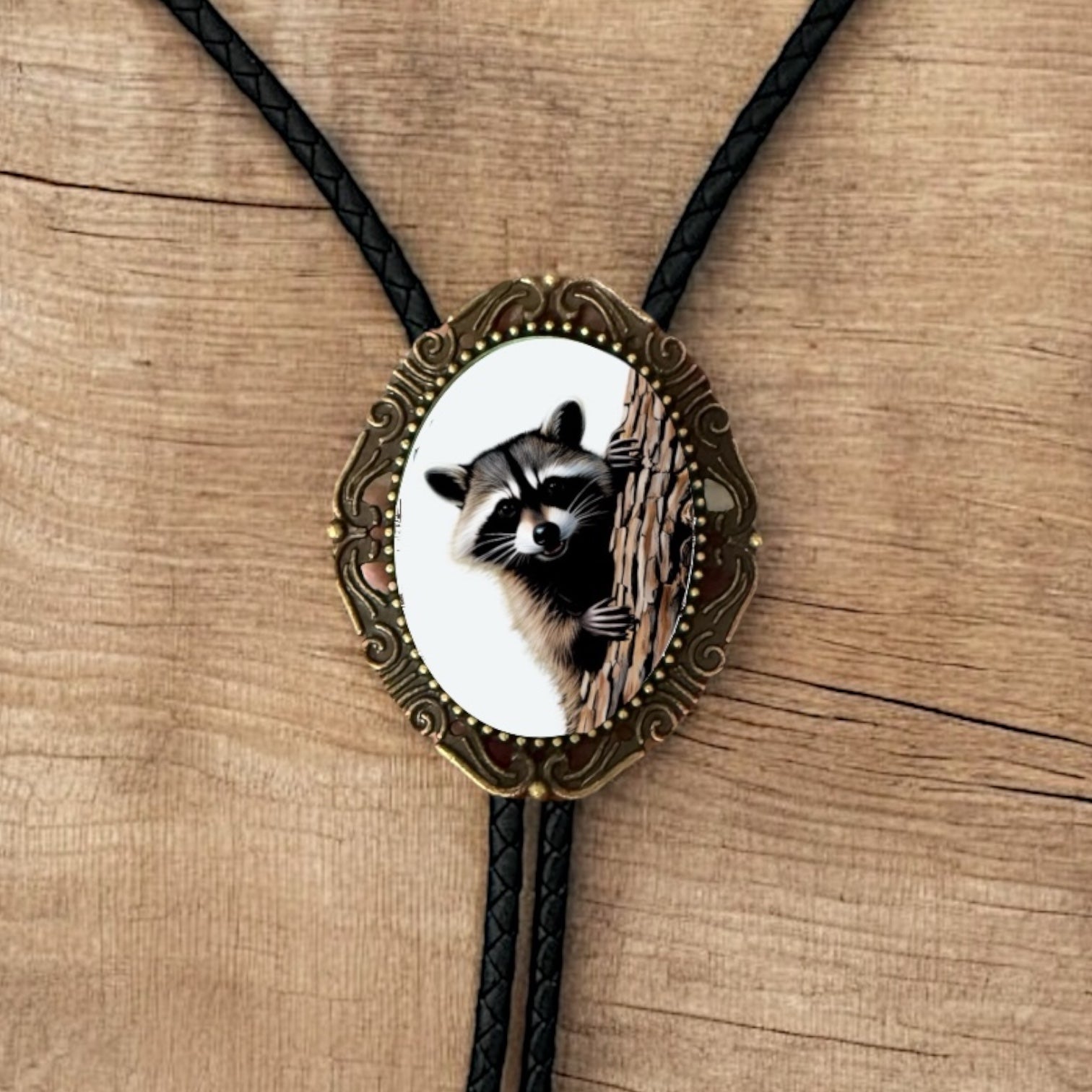 Western Bolo Tie with Raccoon with black leather cord on a wooden table.