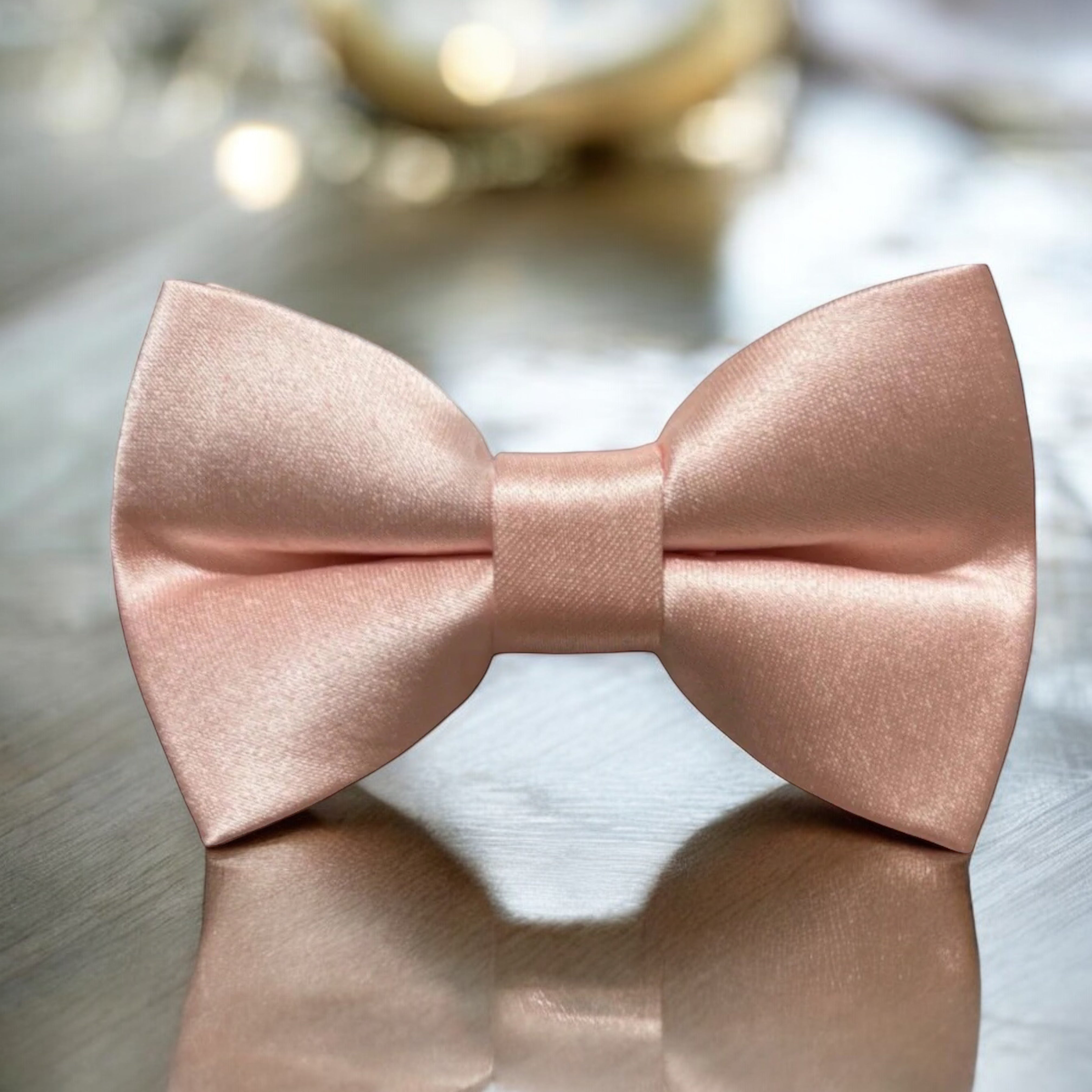 Satin blush pink bow tie for men, groomsmen, wedding party and ring bearers sitting on a mirrored table.