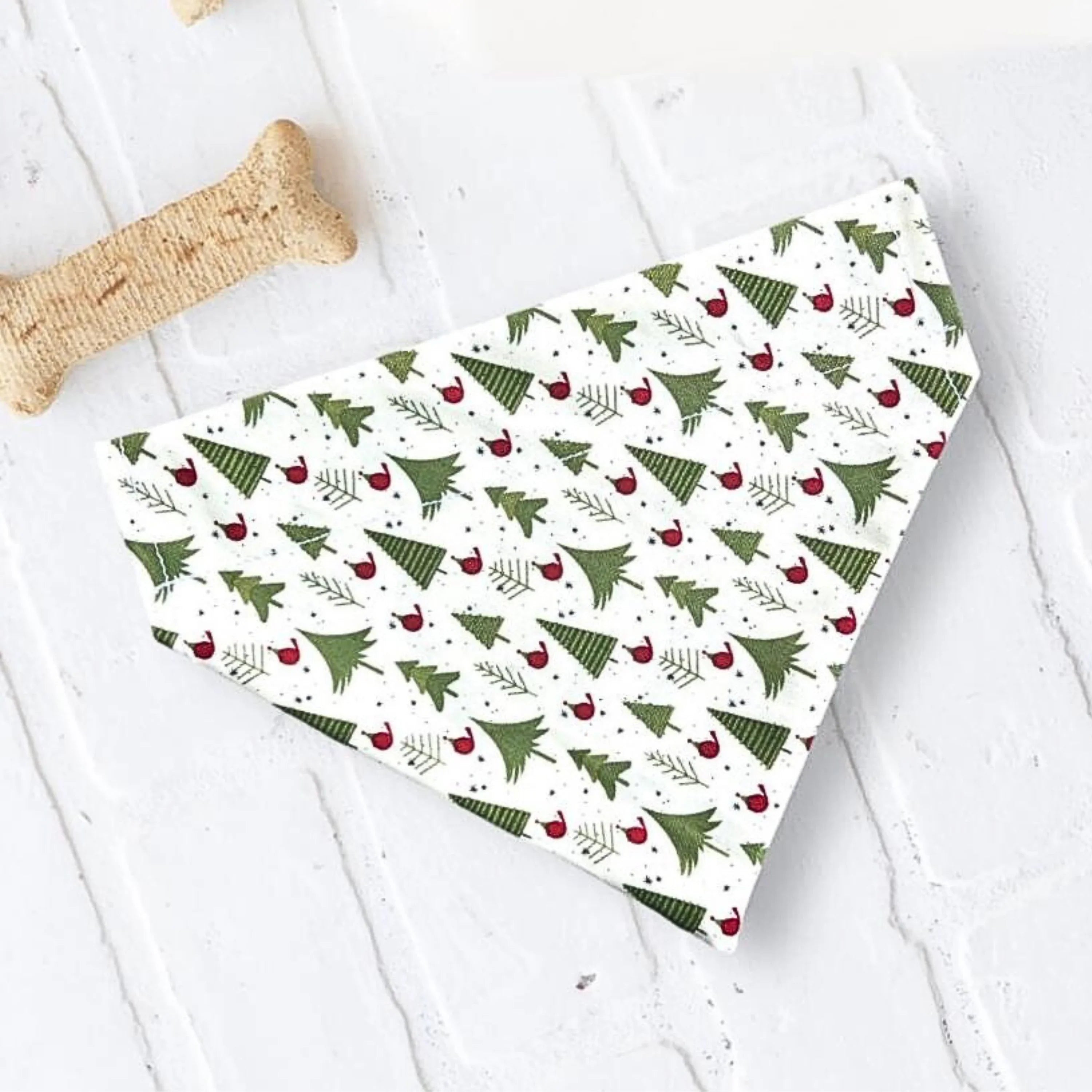 Christmas tree patterned pet bandana on a light surface with a beige bone chew nearby