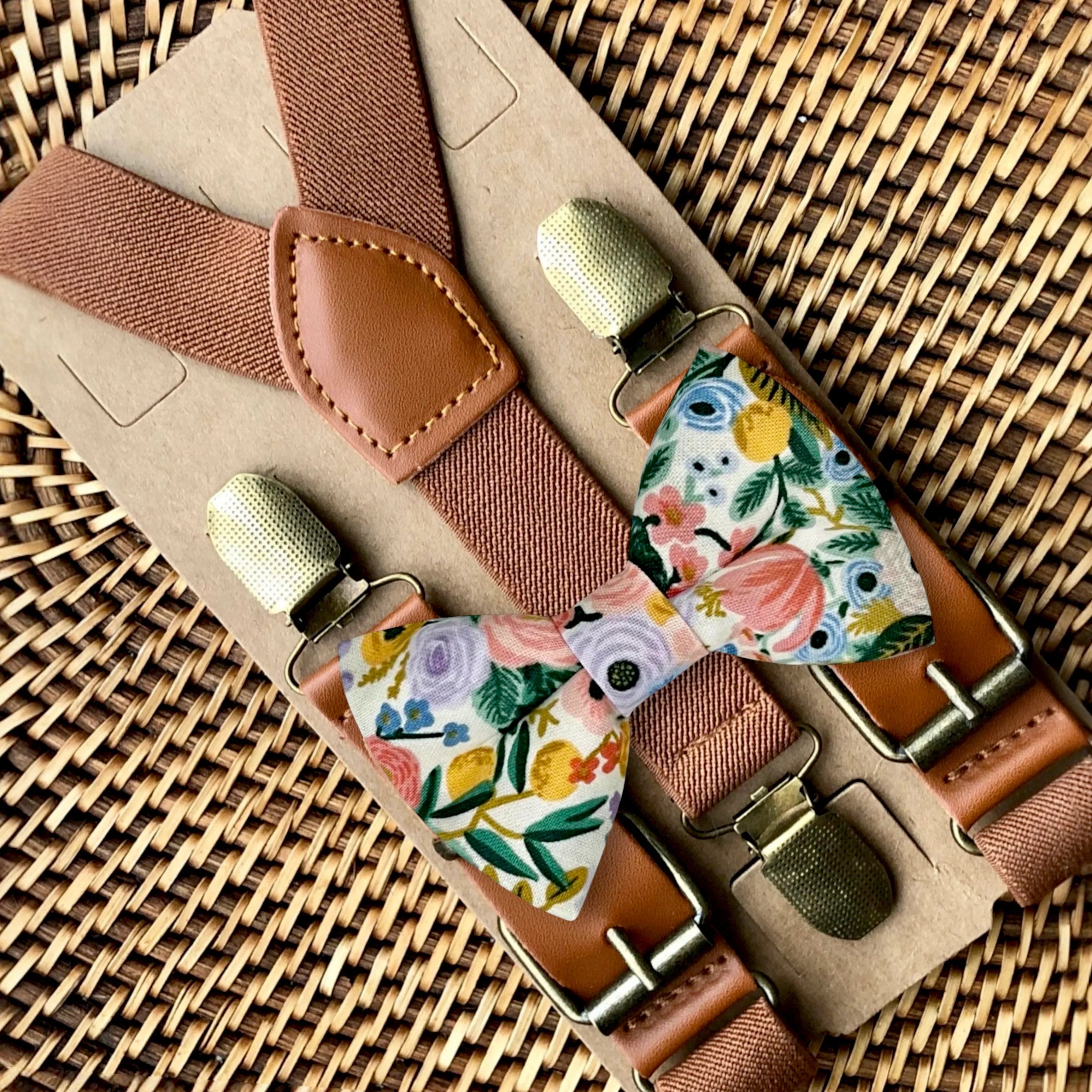 Brown suspenders with a tan leather patch displayed on kraft backing as part of a bow tie and suspenders set