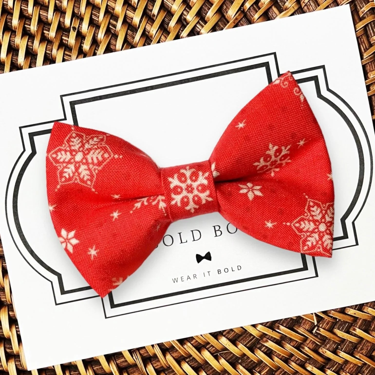 Red snowflake bow tie for dog or cat collar shown on a white card with black border on a woven mat