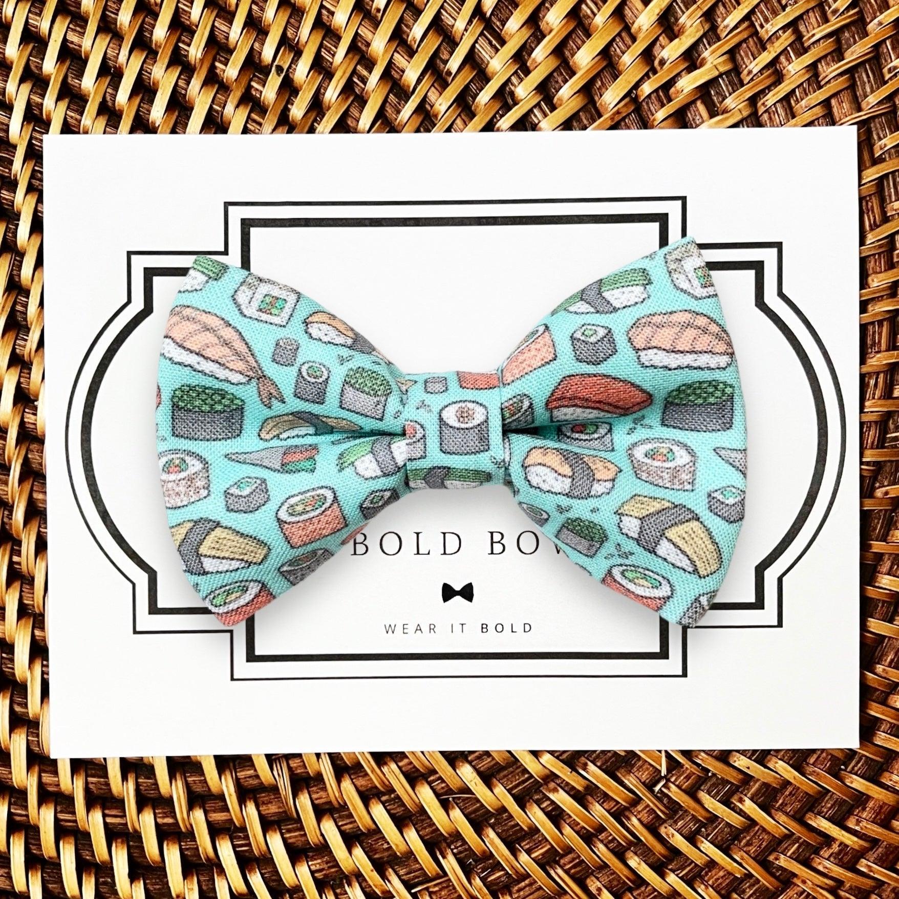 Teal sushi pattern bow tie for pets displayed on a white card with a decorative frame against a woven background