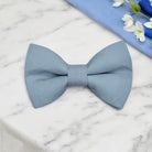 Dusty blue bow tie on a marble surface with a blue cloth and flowers in the background