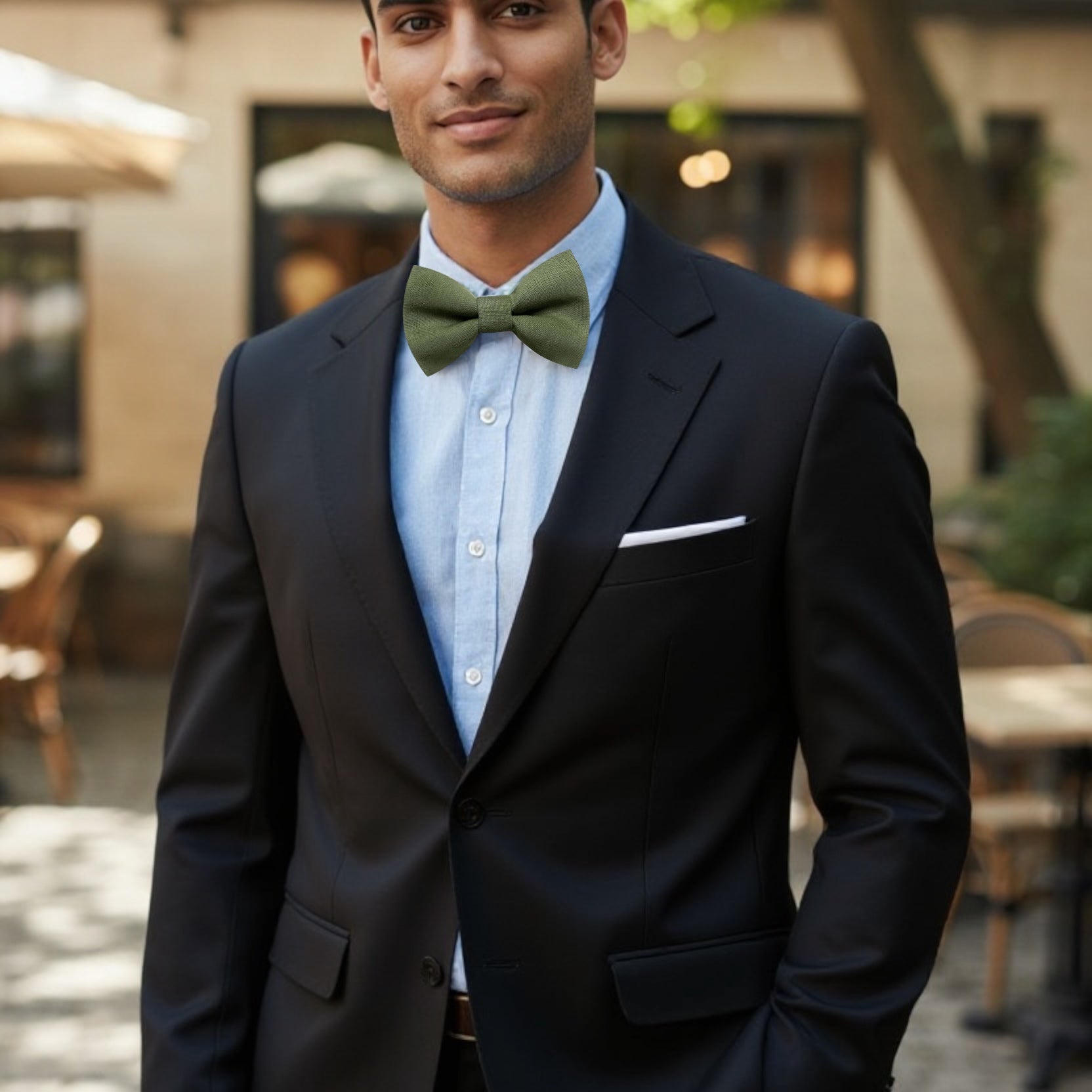 Groomsman in a black suit with an olive green bow tie standing outdoors.
