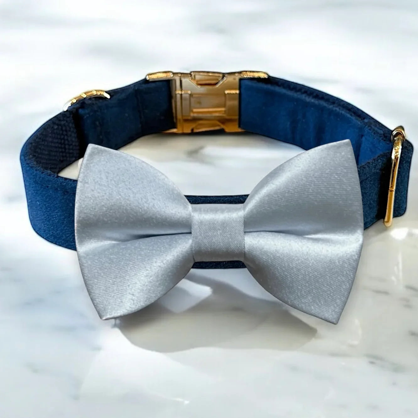 Navy blue velvet dog collar with a light blue dog bow tie on a marble surface