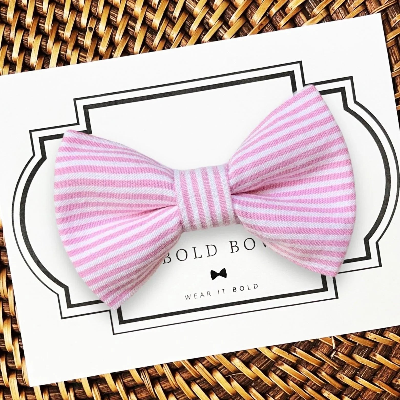 Pink seersucker bow tie displayed on a white card with a decorative frame.