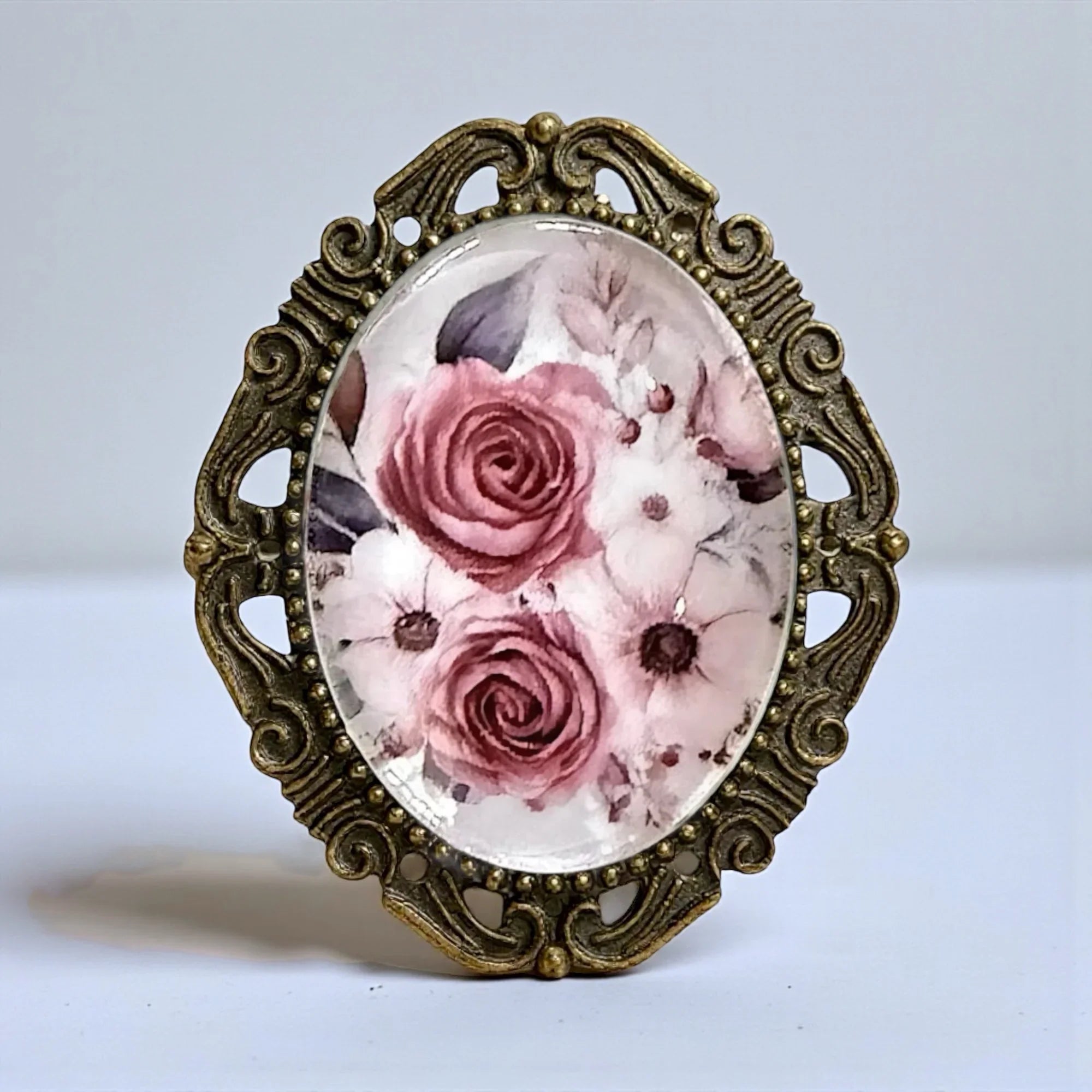 Purple floral brooch with floral design and ornate bronze frame on a light background