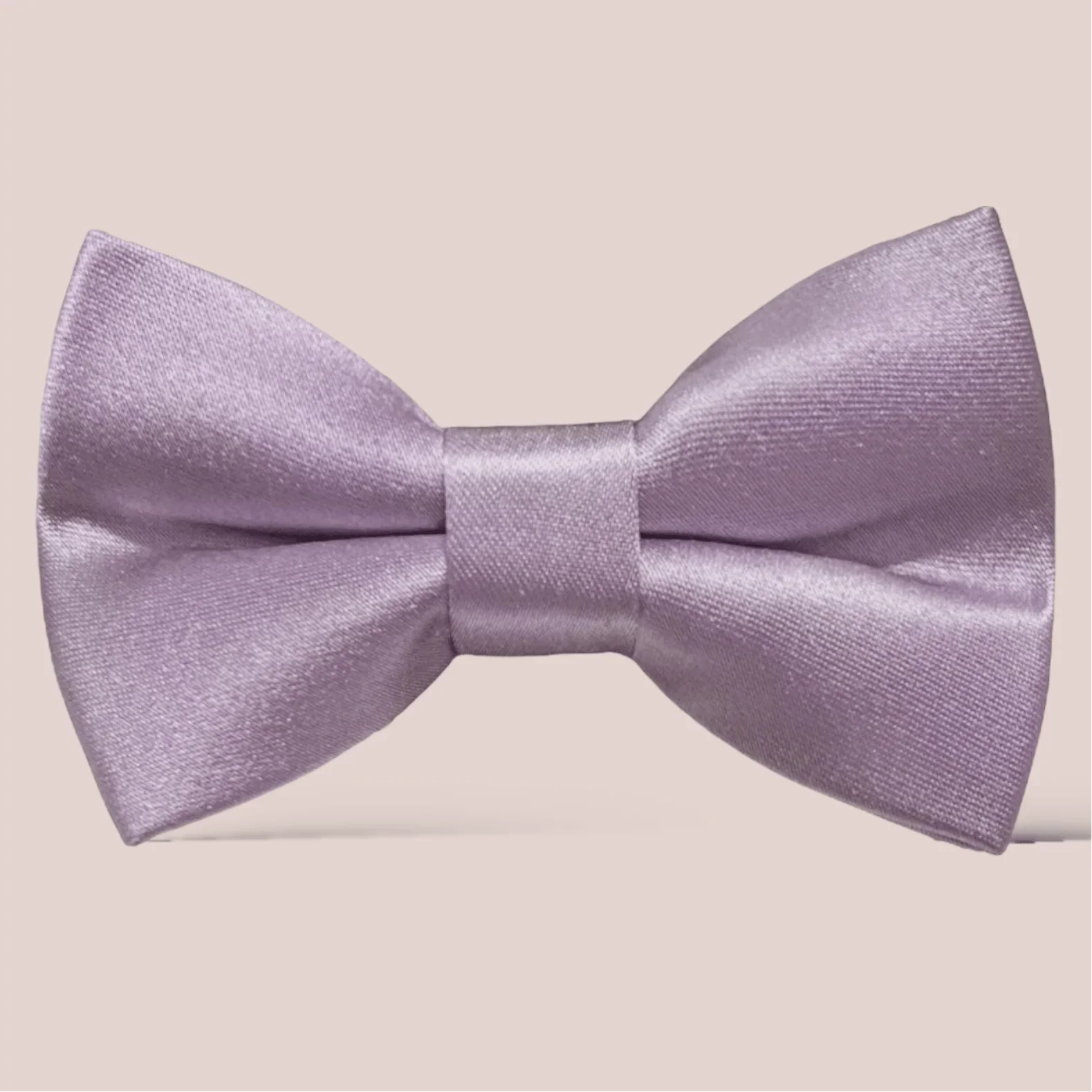 Close up of lavender satin hair bow on a pale beige background.