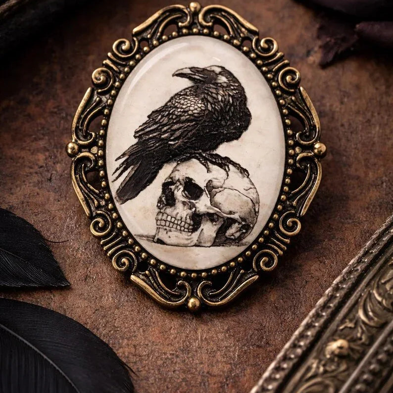 Decorative black bird brooch with a raven and skull design on a textured surface.