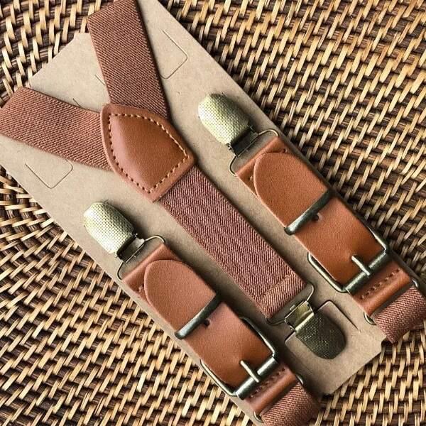 Wedding suspenders for groomsmen and ring bearers with leather accents on a textured surface