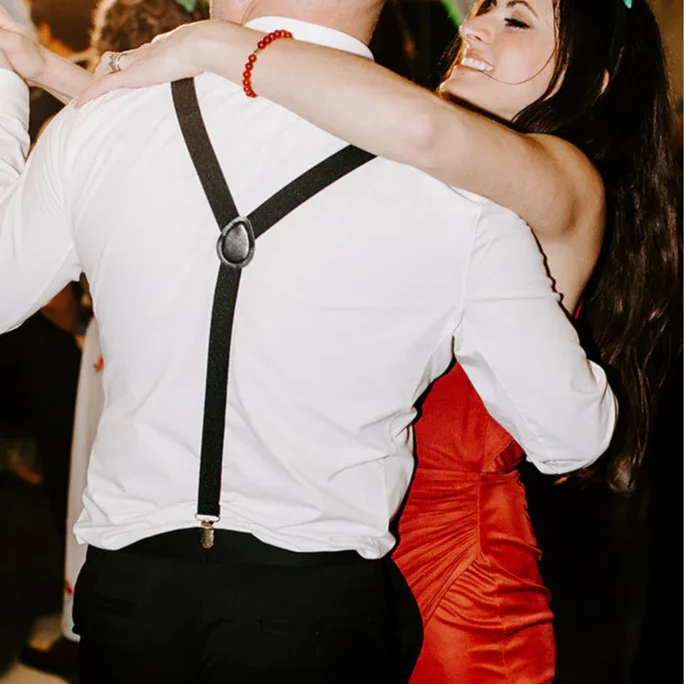 Man dancing with a woman at a wedding in black suspenders, Y-back.