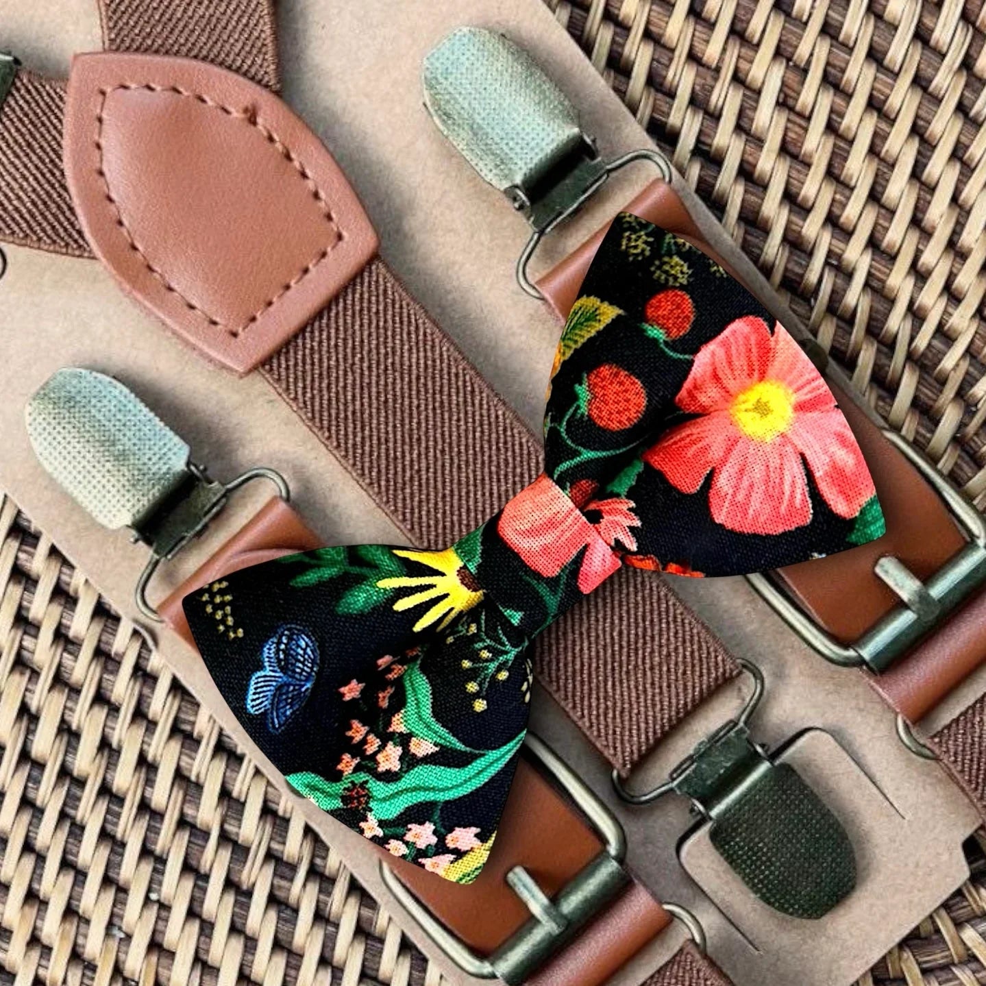 Black floral bow tie with bold multicolored flowers paired with dark brown suspenders.