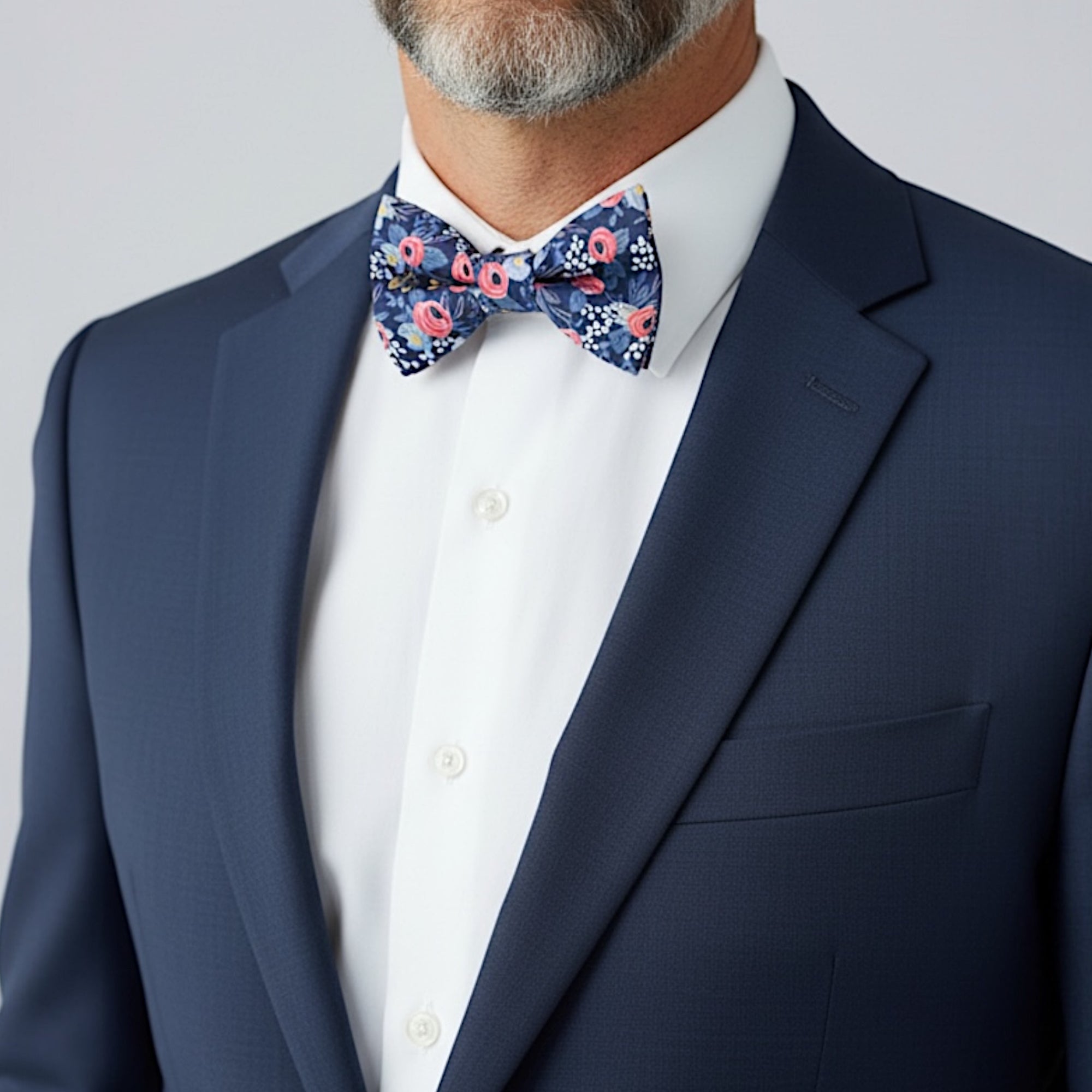 Groomsman wearing a navy floral bow tie in a wedding with a white shirt and suit against a plain background