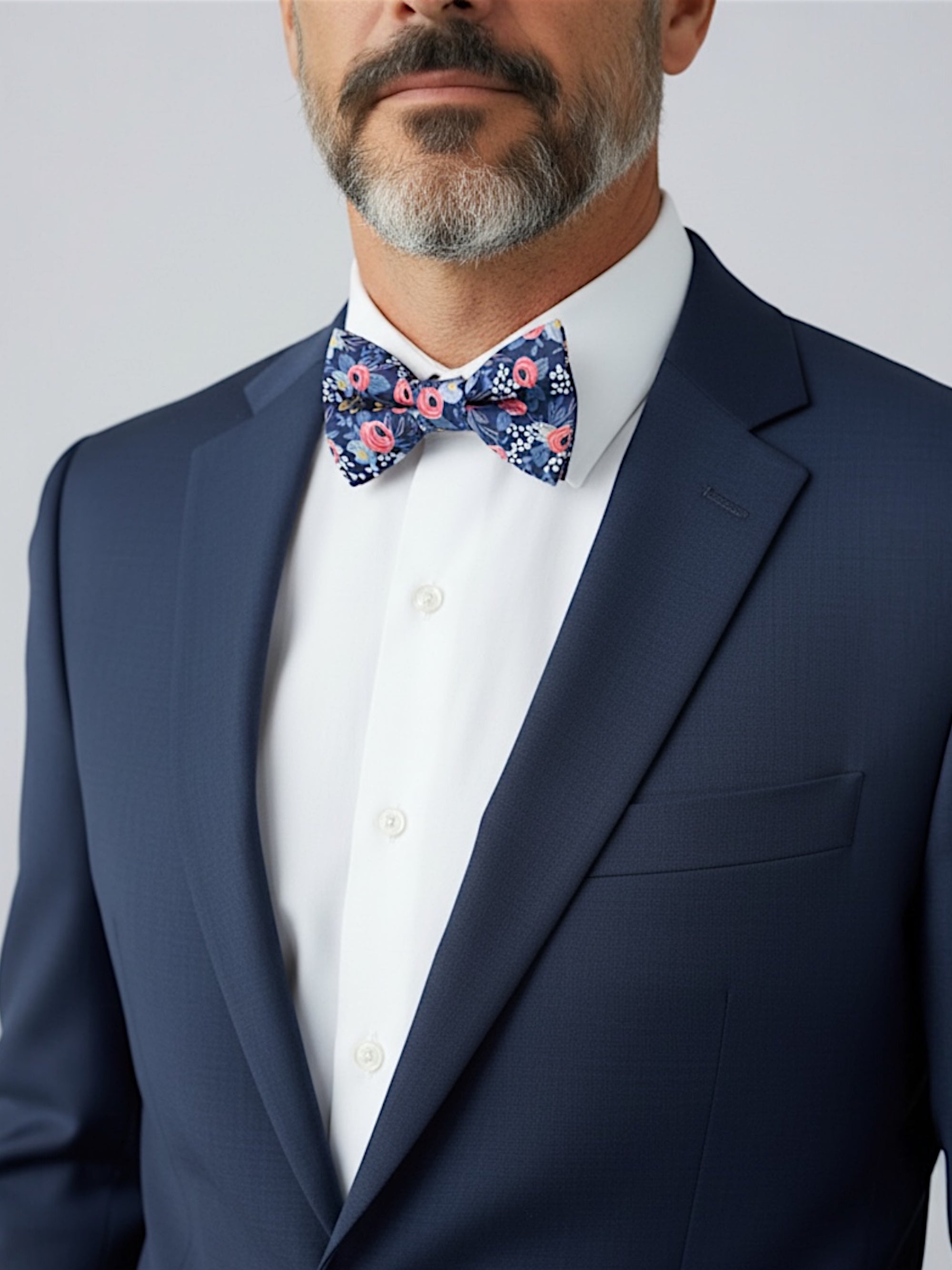 Groomsman wearing a navy floral bow tie in a wedding with a white shirt and suit against a plain background