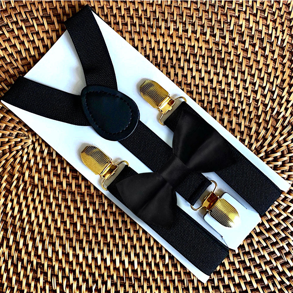 Black suspenders with gold clips on a white box against a woven background