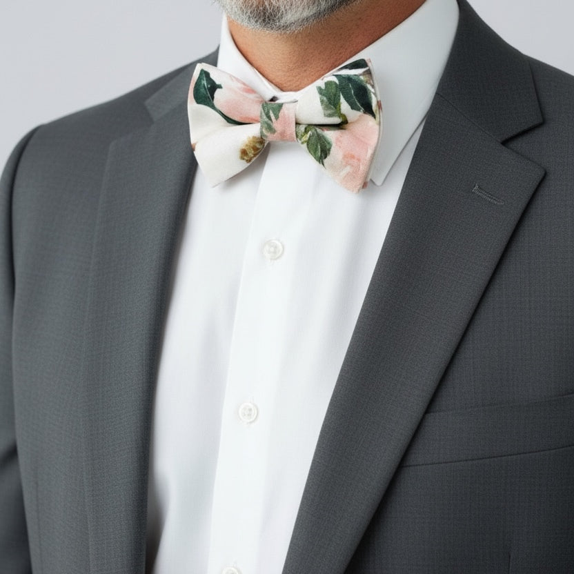 Groomsman wearing a gray suit with a white shirt and white and pink floral bow tie against a light gray background