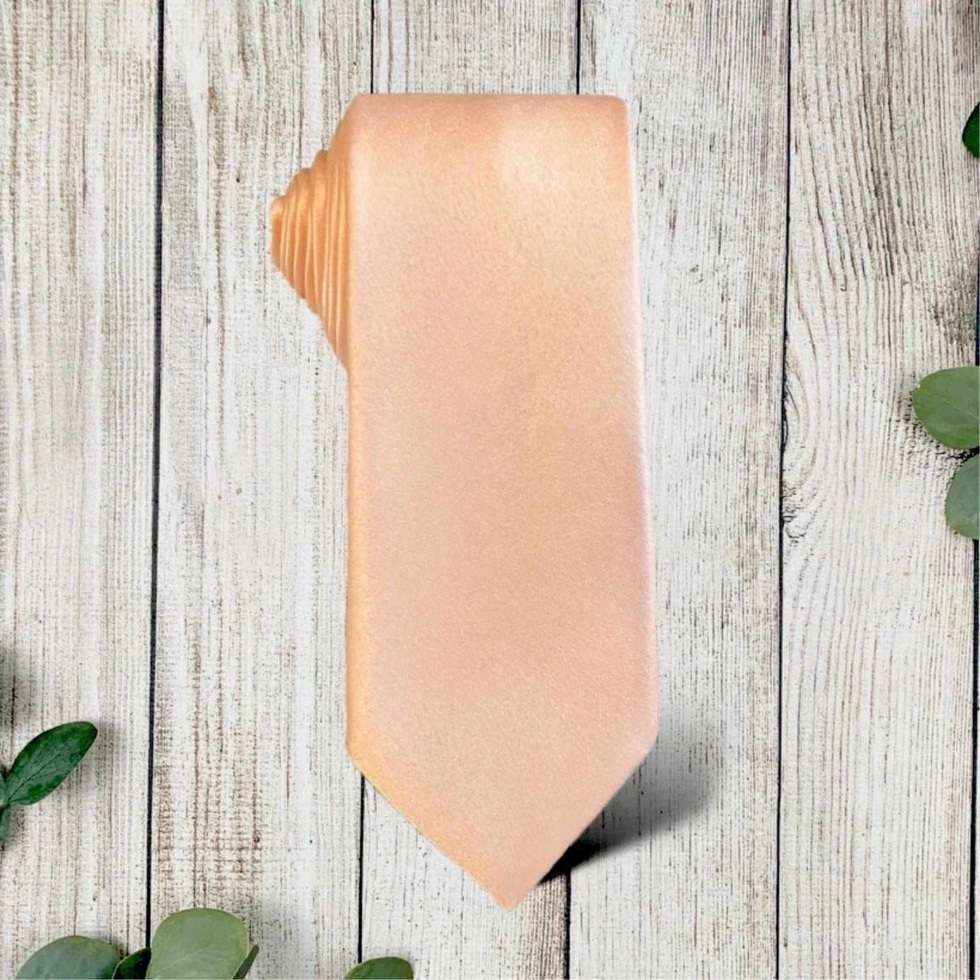 Blush pink satin necktie folded on a rustic wooden surface