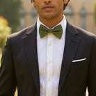 Groomsman wearing a black suit with a white shirt and olive green bow tie outdoors.