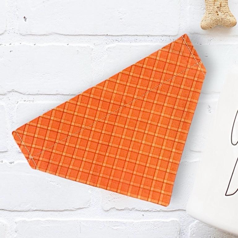 Bright orange plaid dog bandana diagonally placed on a white brick background