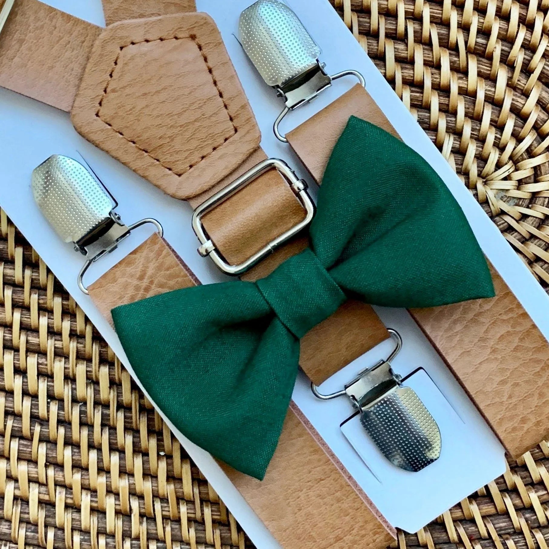Green bow tie and brown suspenders with silver clips on a woven surface