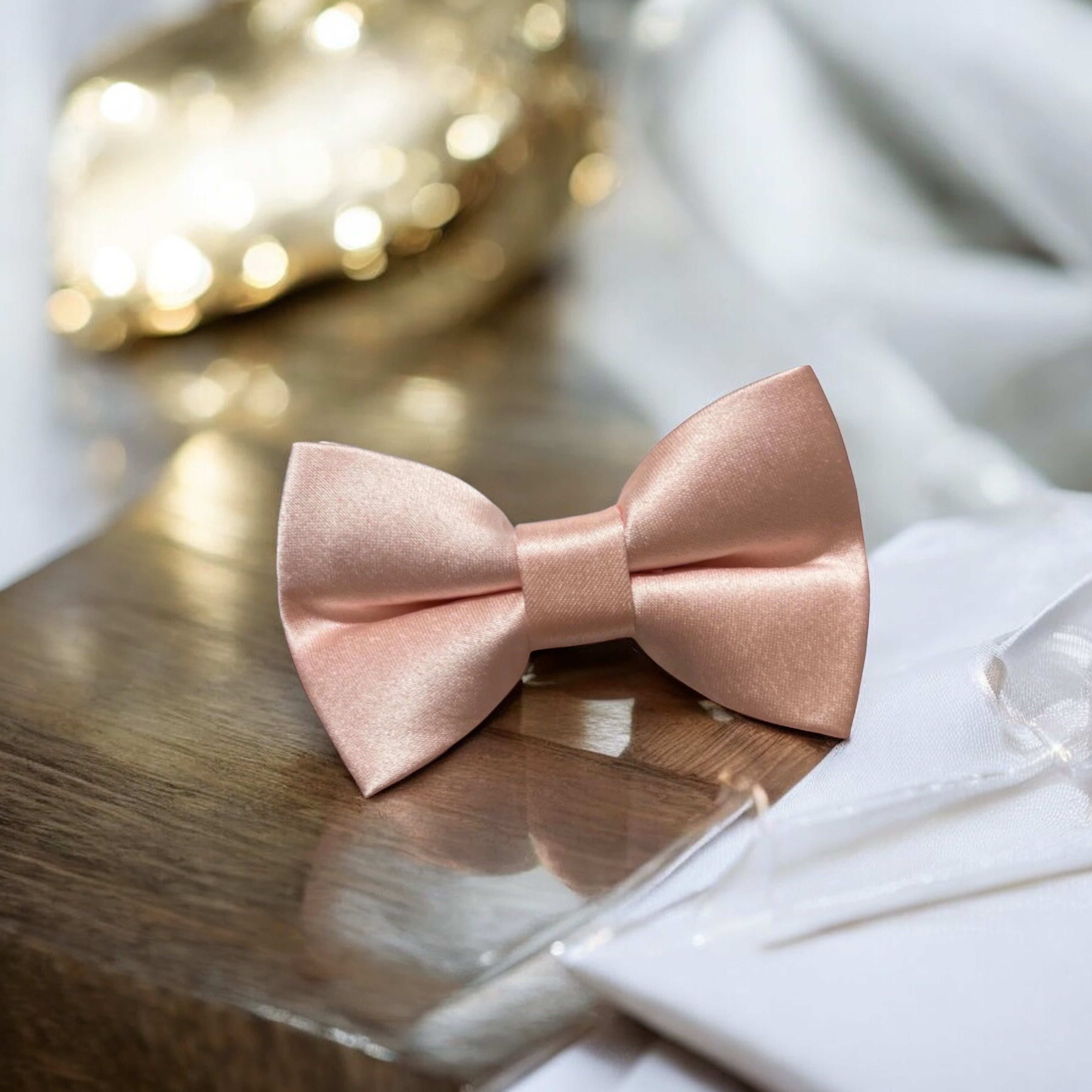 Satin blush pink bow tie for men, groomsmen, wedding party and ring bearers sitting on a wooden table.