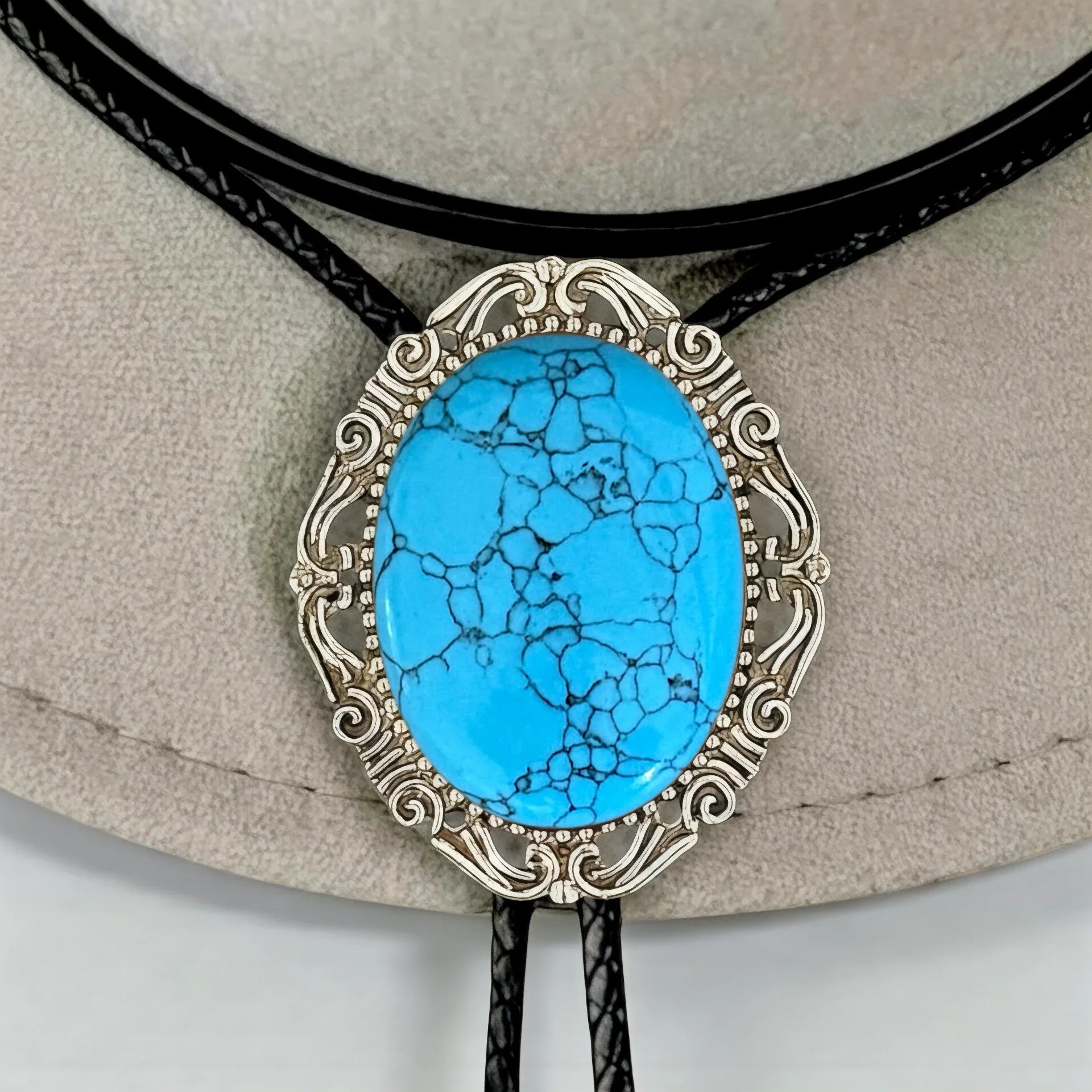 Infographic from The Bold Bow Tie titled Bolo Tie Features. Right: A vintage-style bolo tie with a blue and white cowboy riding a horse illustration inside an ornate bronze filigree frame on a black braided cord. Left: Lines connect the image to three checkmark features: Handmade, 39" Long Cord, and Pendant is 1.5" (L) x 1.25" (W). Bottom text reads Perfect Addition to Your Outfit.