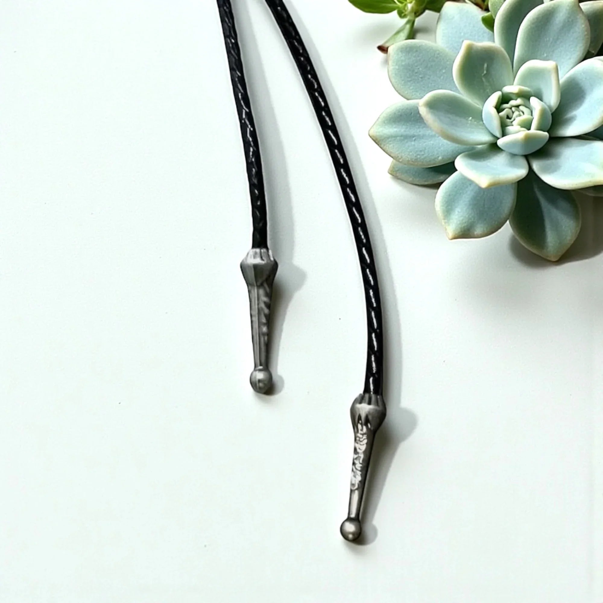 Bolo tie silver tips shown on a white table and flower.