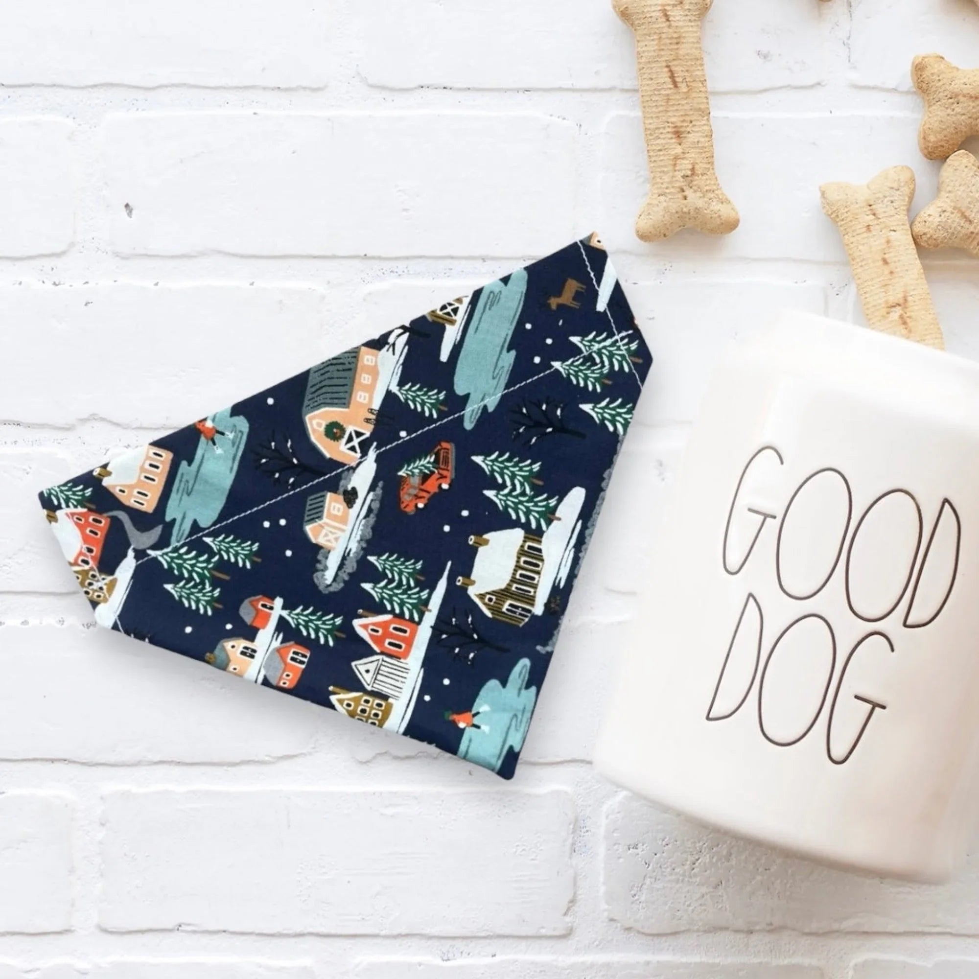 Navy blue Christmas dog bandana with a festive village and trees print laid on a white surface.
